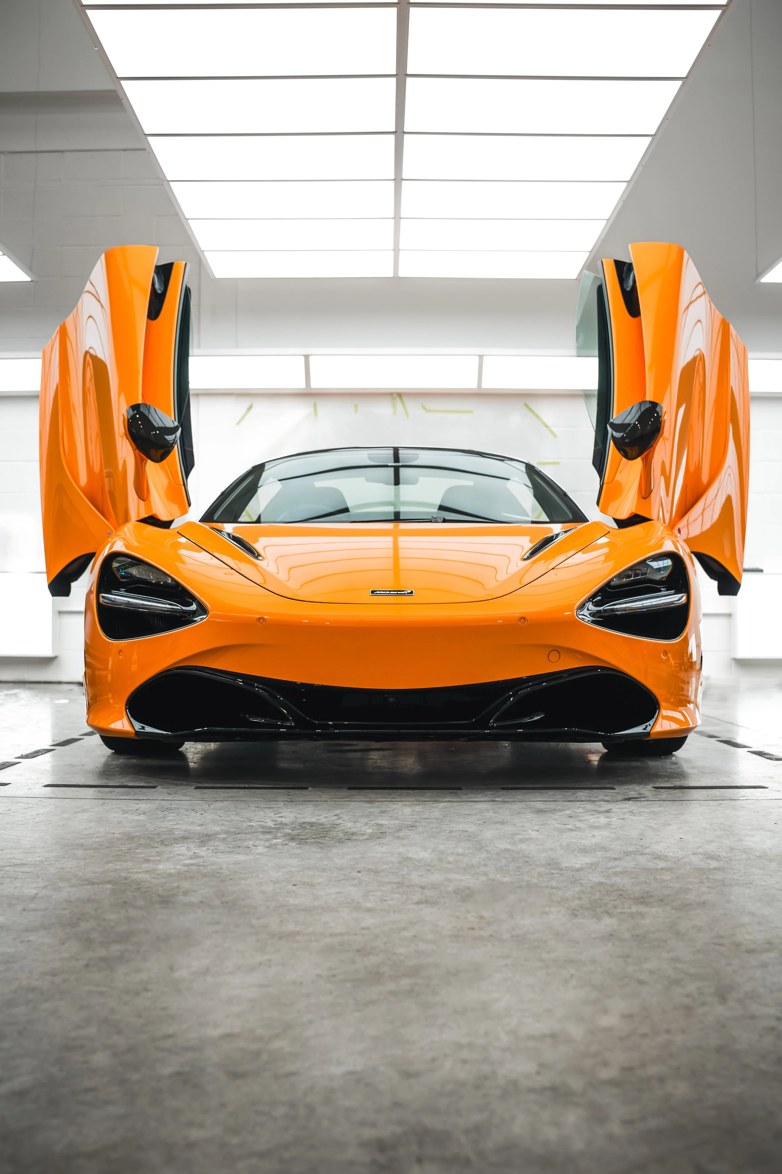 Front view of an orange sports car with gullwing doors open in a garage.