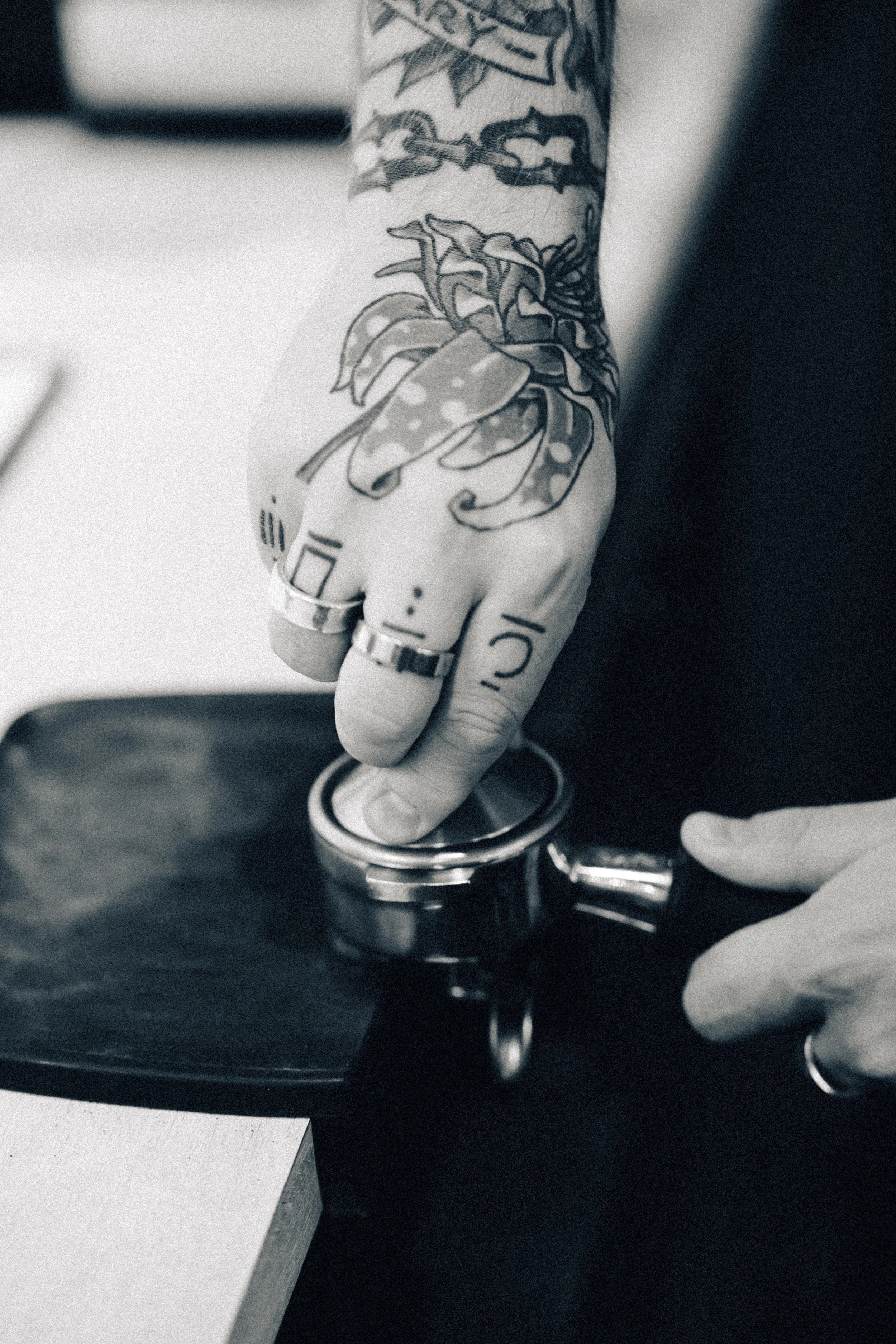 A tattooed hand with rings on fingers, pressing a button on a coin-operated machine, seen in black and white.
