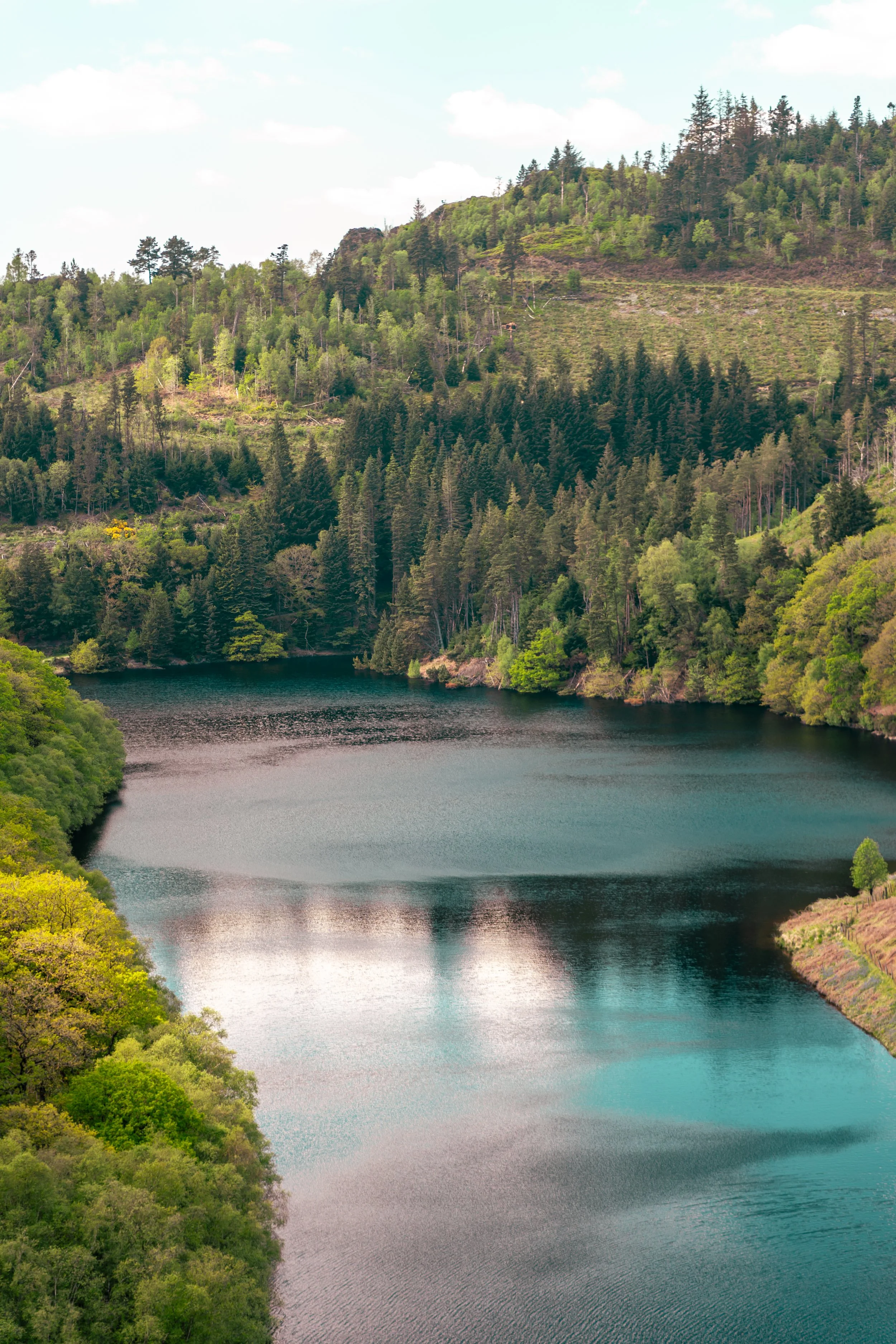 A scenic view of a river surrounded by lush green forested hills under a partly cloudy sky.