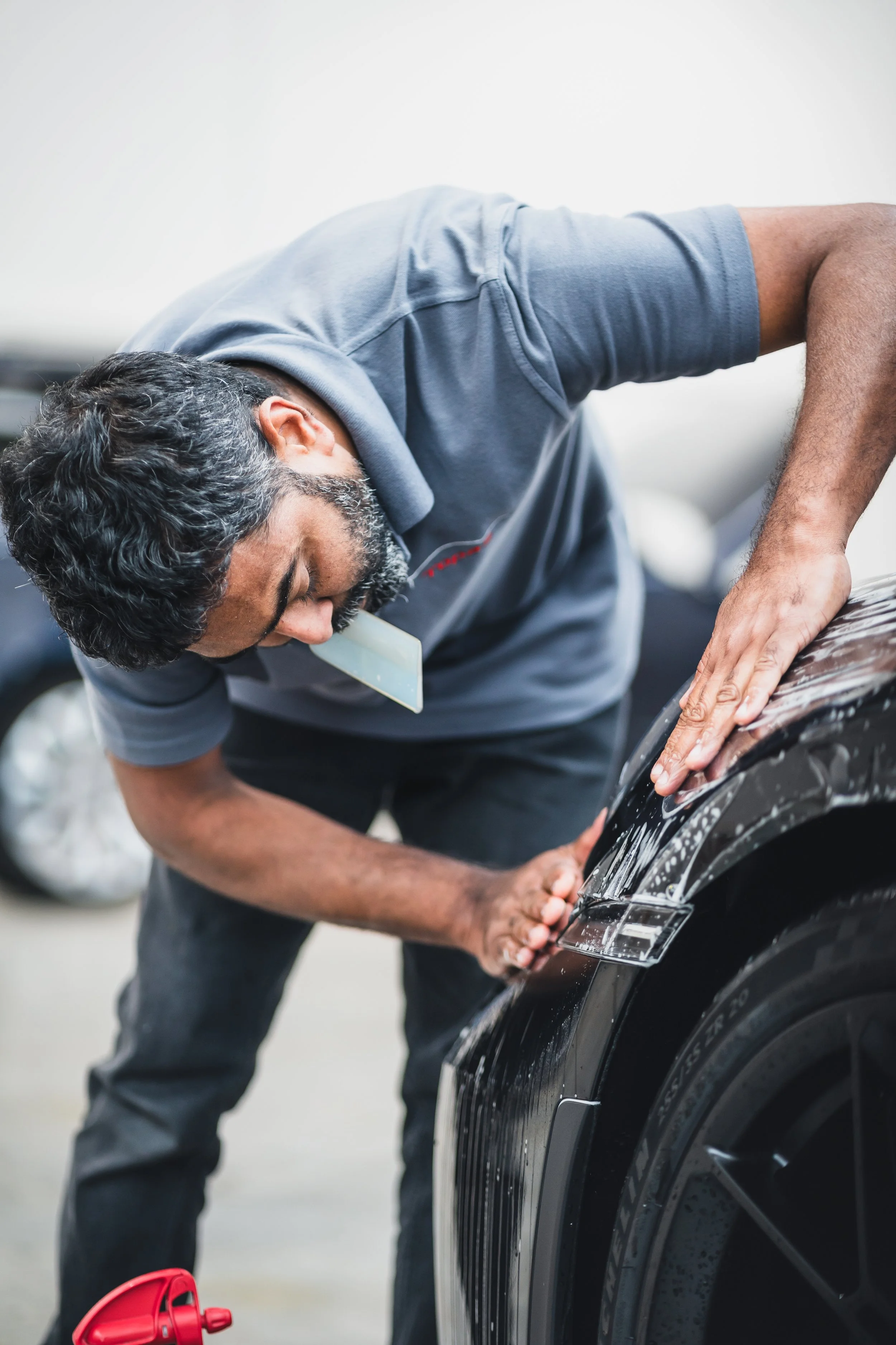 Man with a beard washing a black car with soap and a sponge in a garage.