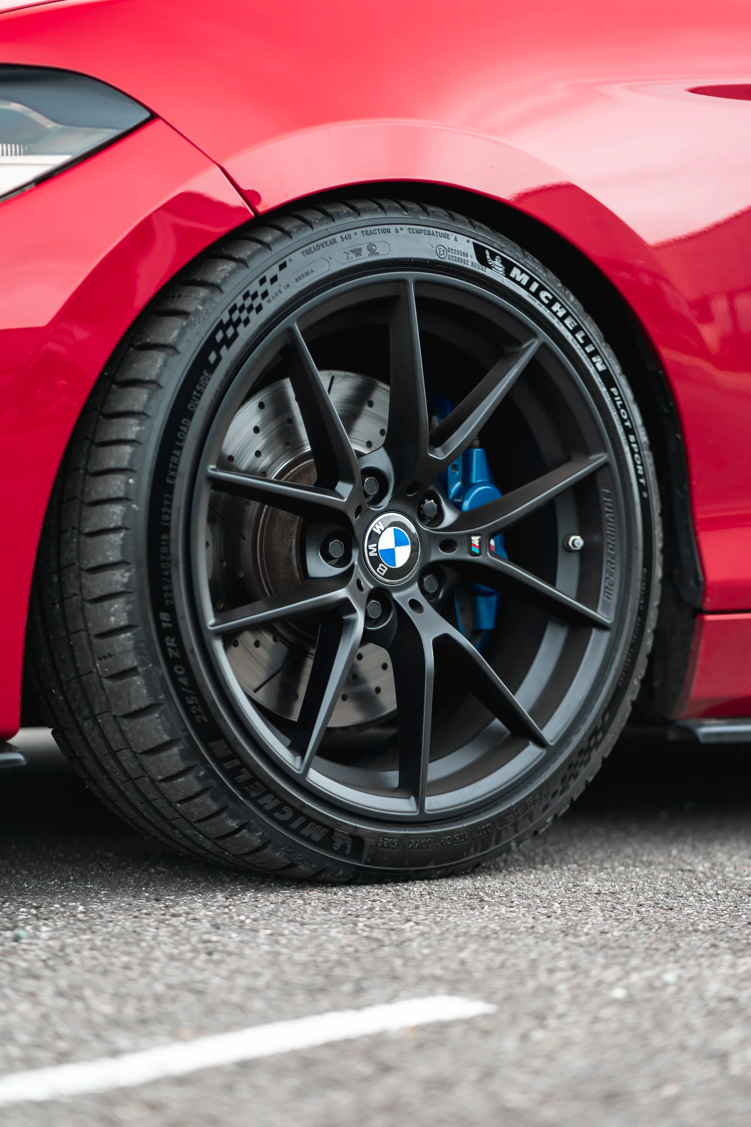 Close-up of a red sports car's front wheel with BMW logo, black alloy rim, and blue brake caliper, parked on asphalt.
