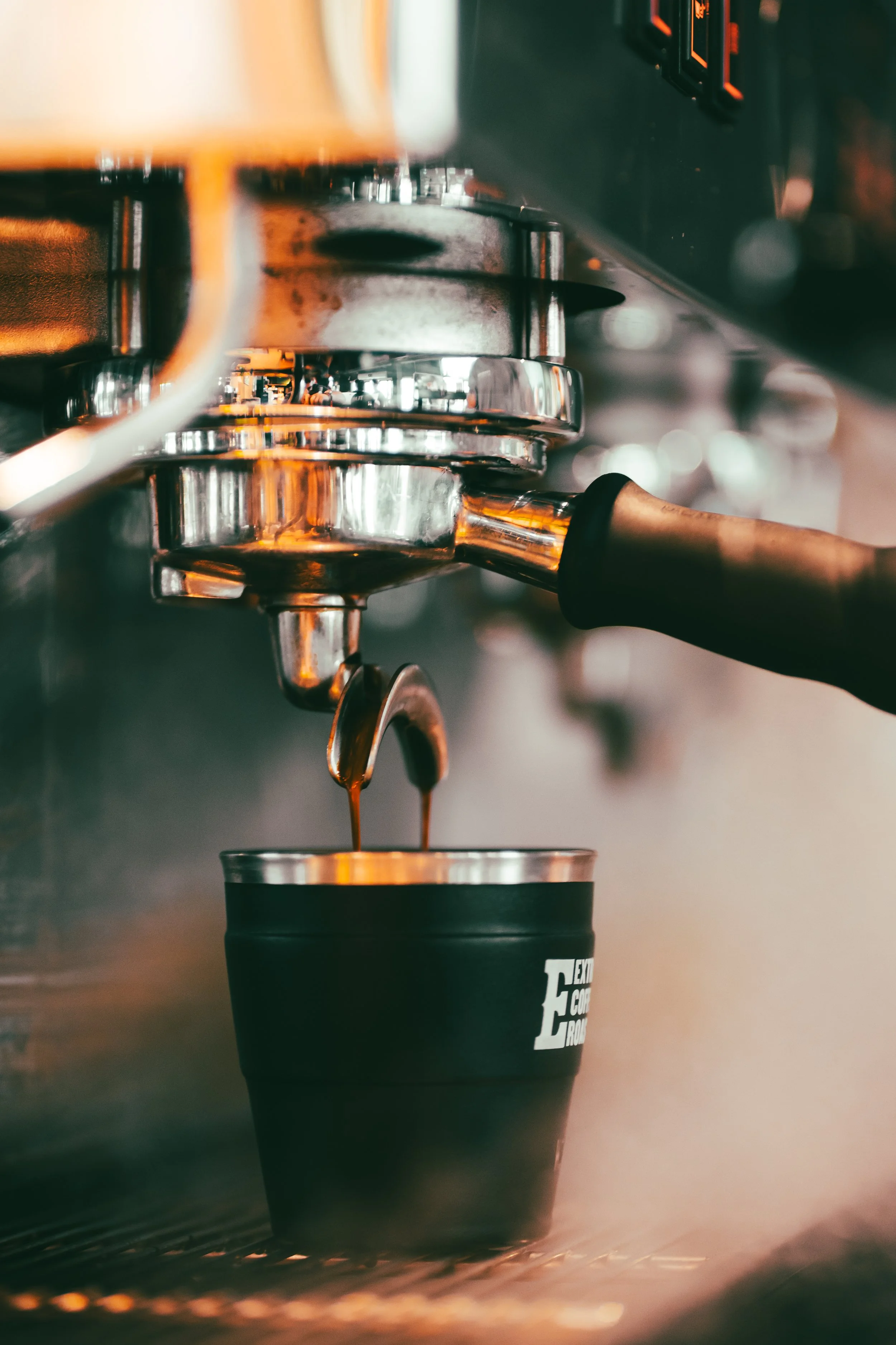 Close-up of a coffee machine pouring brewed coffee into a black cup with a logo, in a coffee shop.