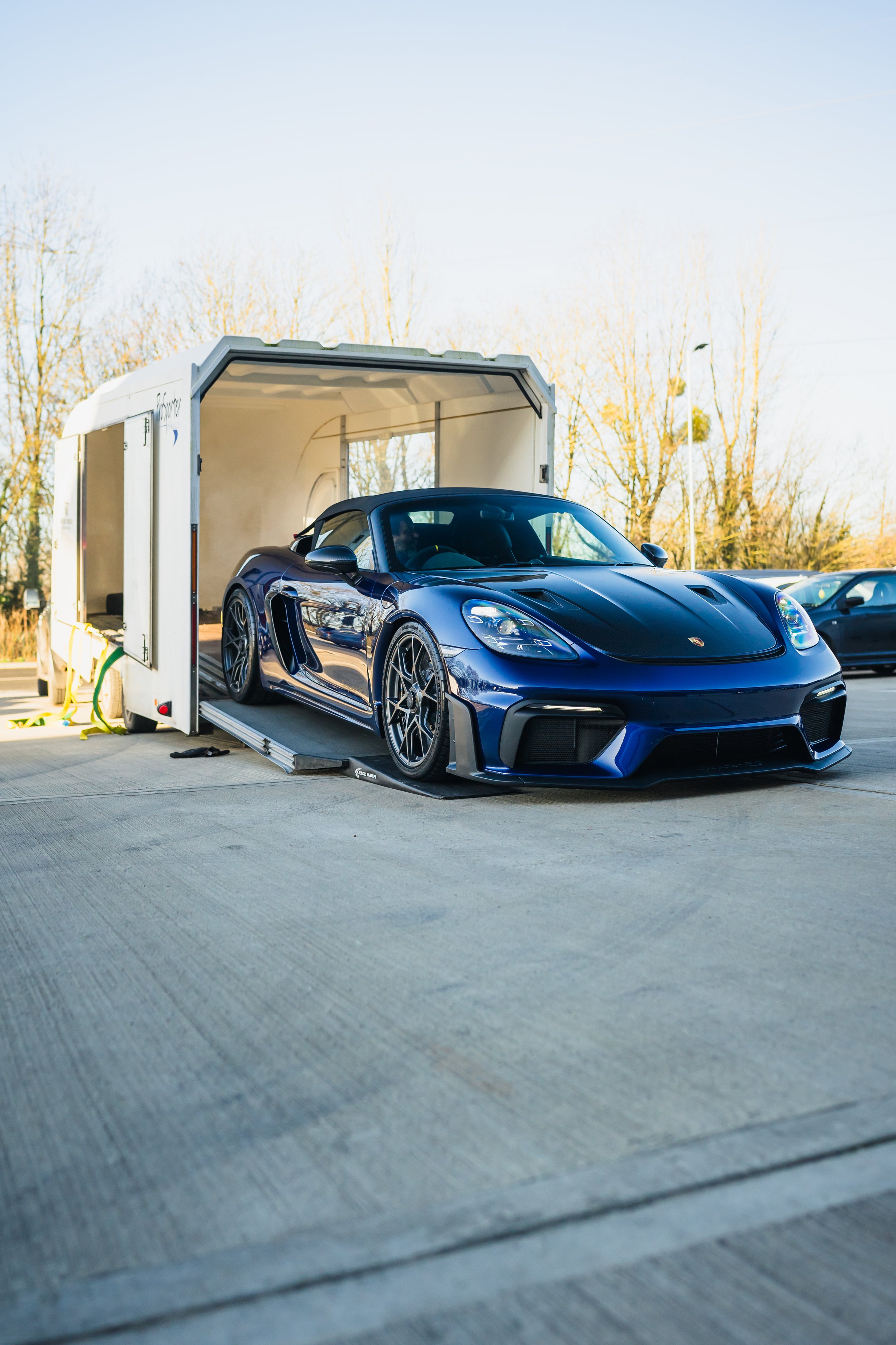 A blue sports car inside a car trailer on a parking lot.