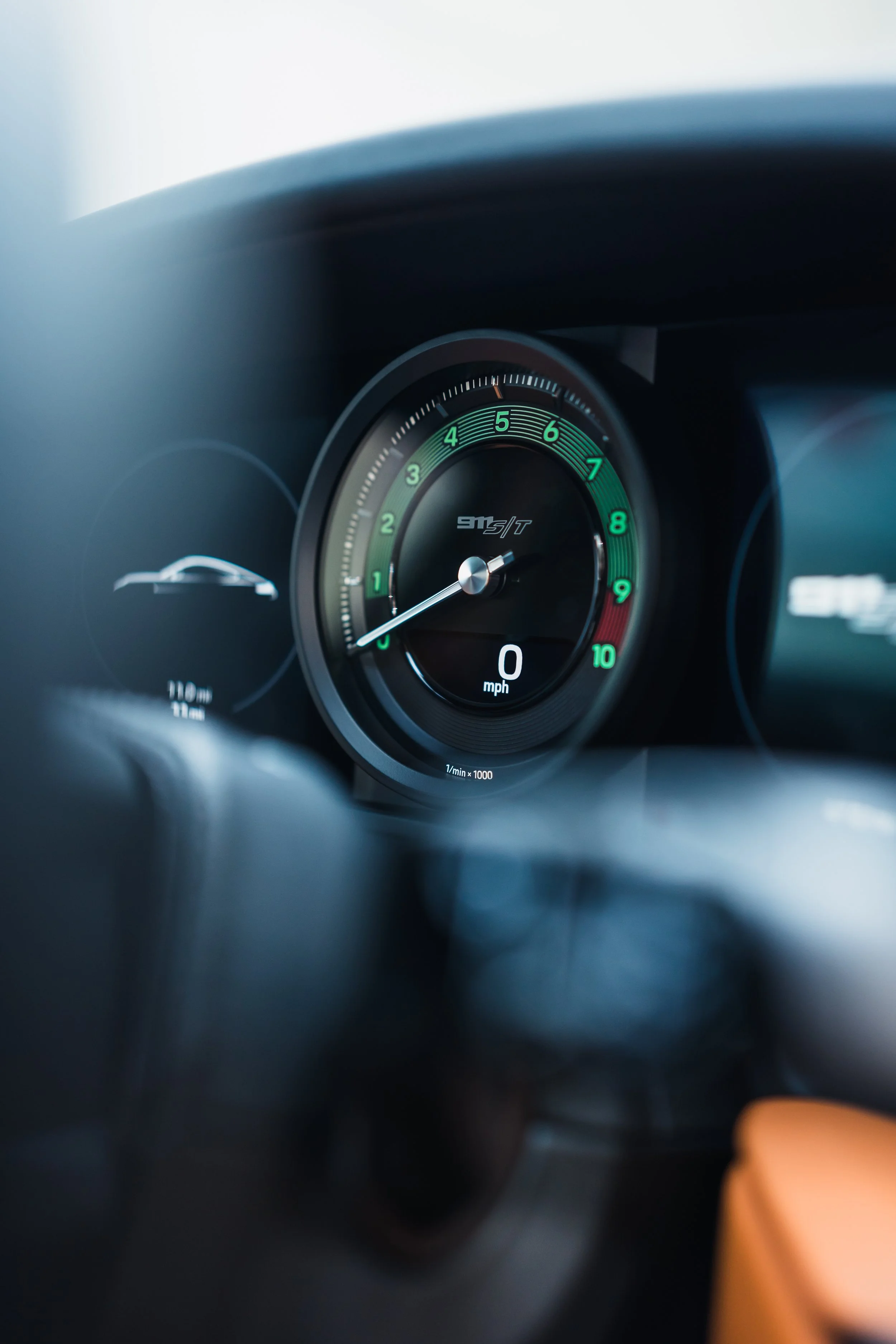 Close-up photo of a car's dashboard showing the tachometer with the needle pointing at 1,000 RPM, and the speedometer displaying 0 mph.