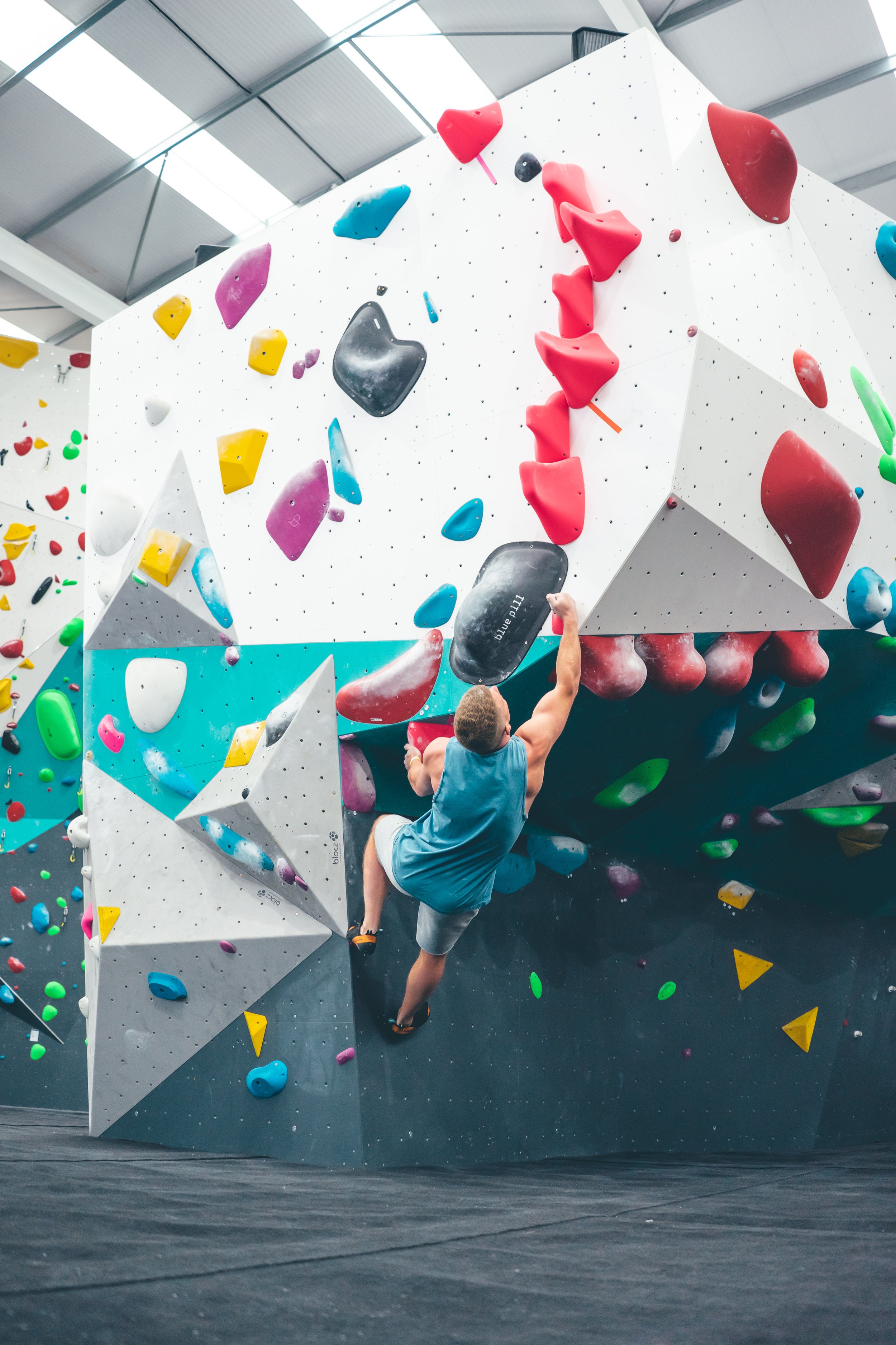 A man bouldering on a colorful indoor climbing wall with holds in various shapes and colors.