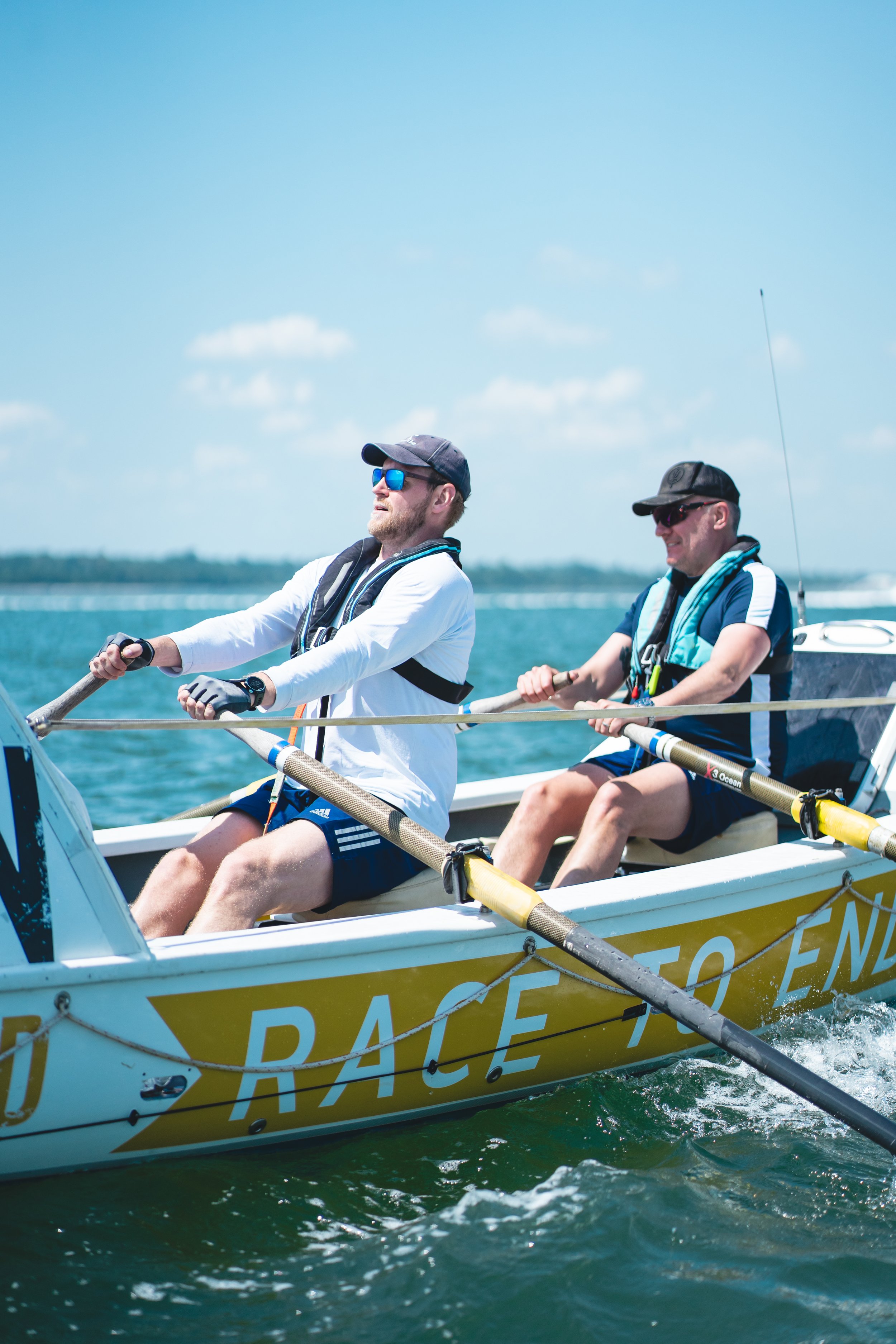 Two men rowing a boat on the water under a clear blue sky