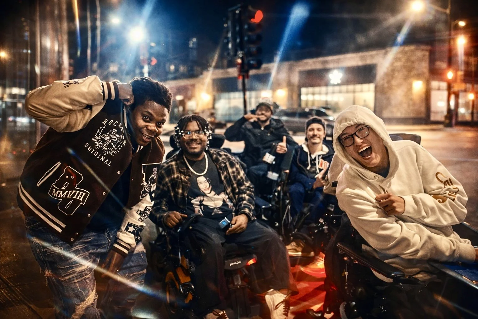 Group of diverse friends enjoying a night out on the street, some sitting in wheelchairs, smiling and laughing at night, with city lights and buildings in the background.