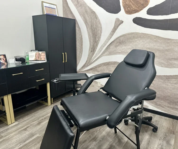 Medical examination room with a black examination chair, a cabinet, a desk, and wall art with abstract floral design.