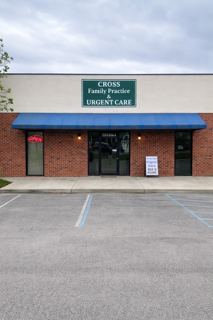 Exterior view of a family practice medical clinic with a green sign reading 'CROSS Family Practice Urgent Care' above the entrance, and a small white sign on the sidewalk.