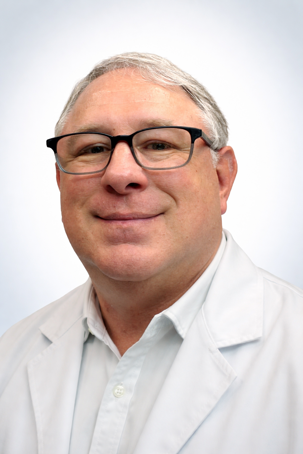 Close-up portrait of a middle-aged man with gray hair and glasses, smiling, wearing a white lab coat against a plain white background.