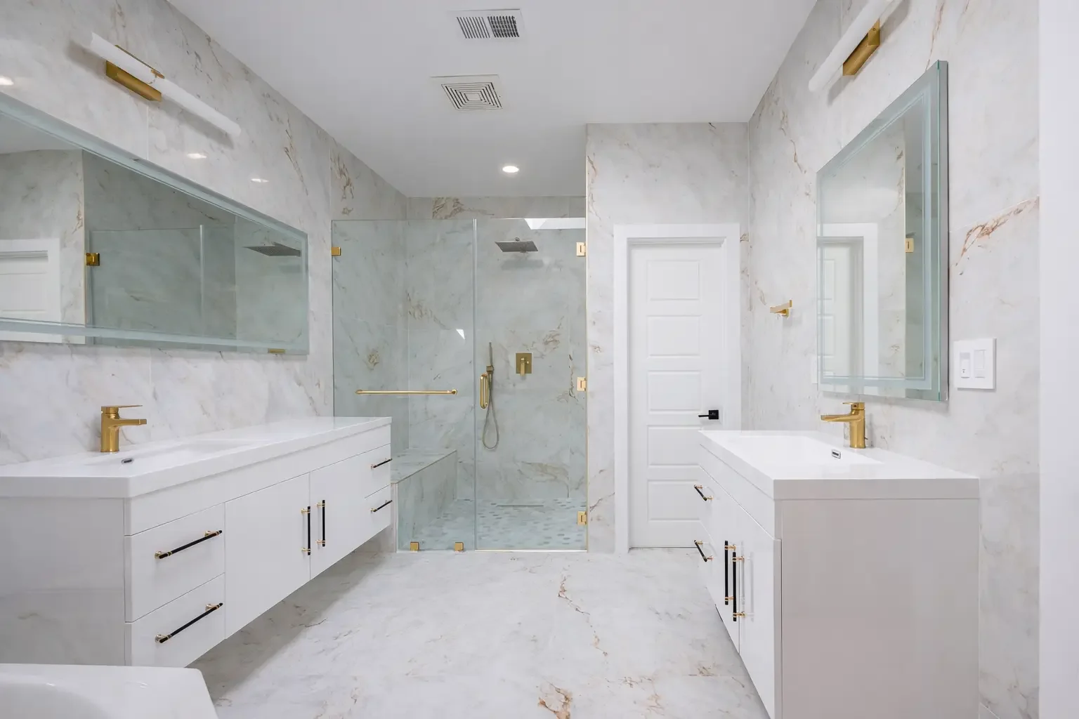 A luxurious white and gold modern bathroom with dual vanities, large mirrors, a glass-enclosed walk-in shower with gold fixtures, and marble walls and floors.