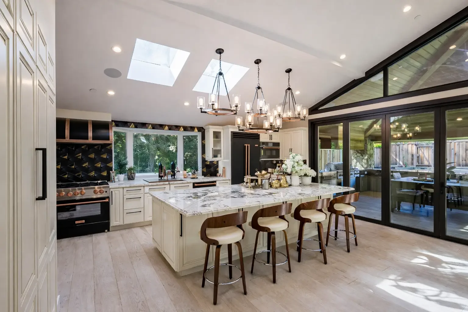 Modern kitchen with large island, chandelier, skylights, and sliding glass doors leading to an outdoor patio.