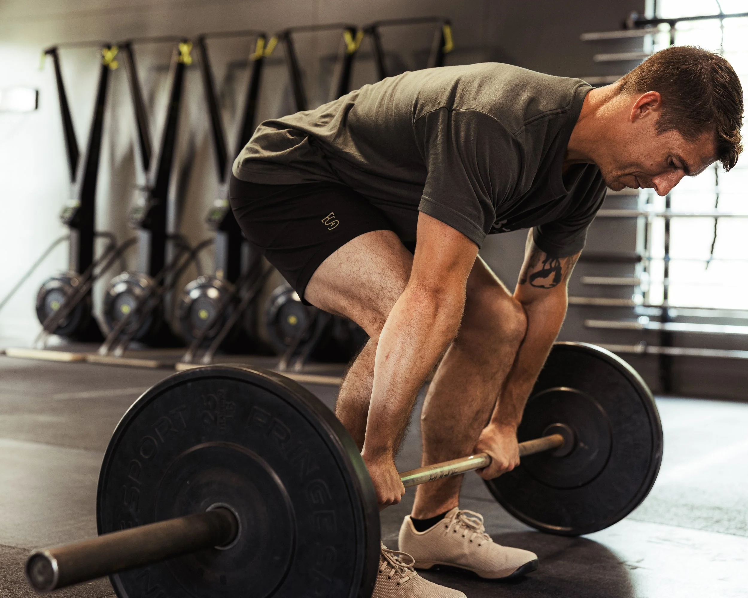 A man in a gym, bending over a barbell with weights, preparing to lift during a workout.