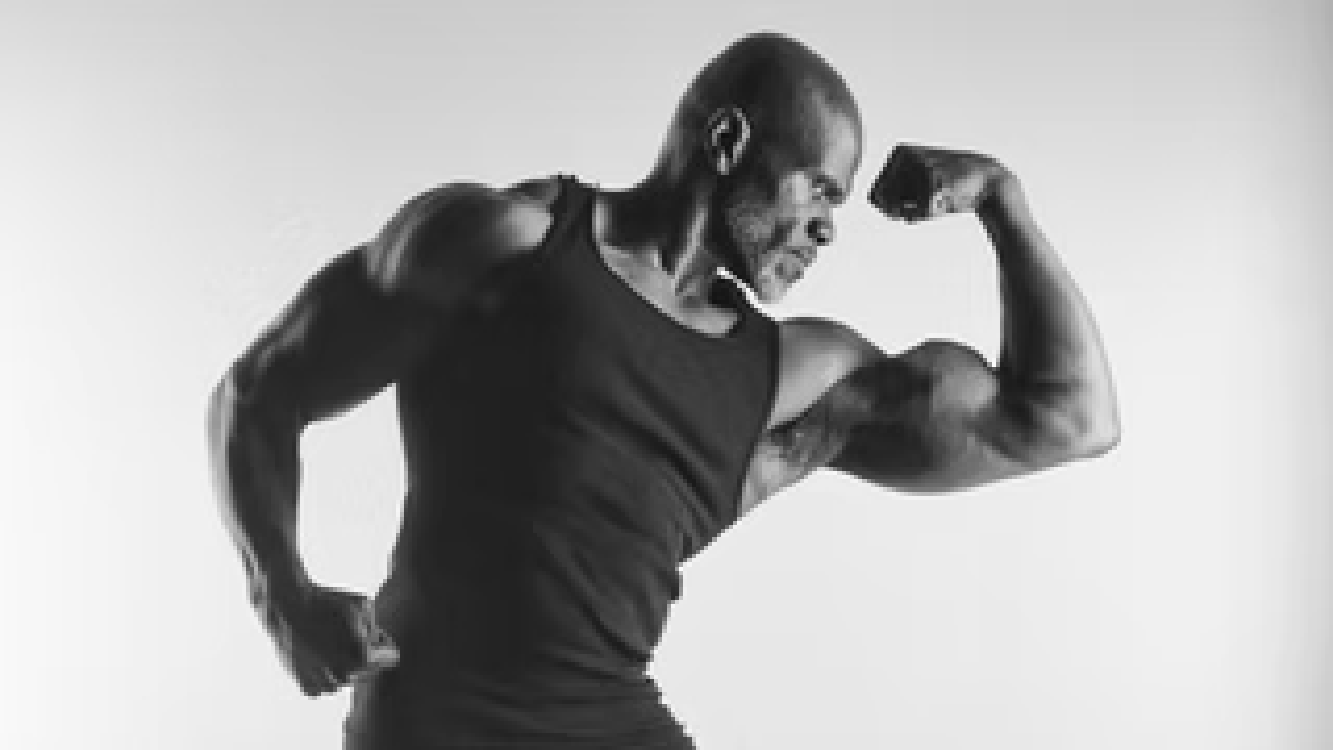 Black and white photo of a muscular man flexing his bicep, wearing a sleeveless shirt. Benny Mobley Public Speaker Emcee Podcast Coach Washington training on on one mentorship