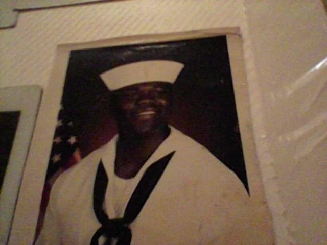 A poster of a smiling person in a Navy uniform with a sailor's hat, with part of an American flag visible in the background. Benny Mobley Public Speaker Emcee Podcast Coach Washington training on on one mentorship