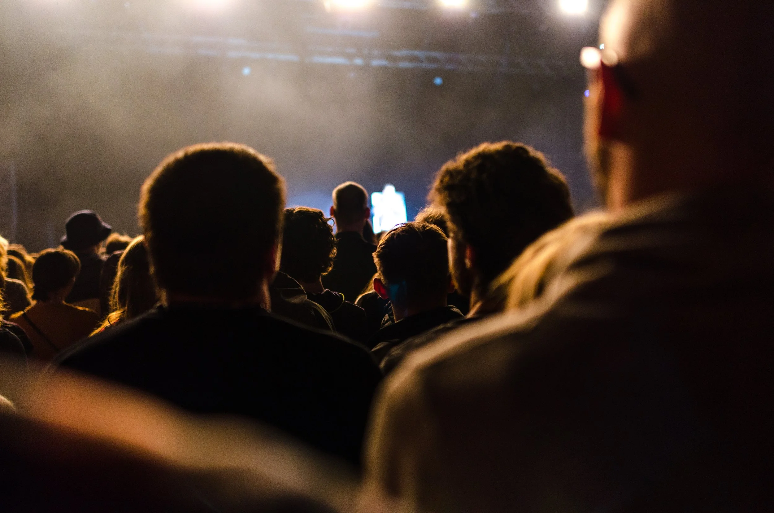 Audience facing a stage with a bright screen, indoors, at a concert or event. Benny Mobley Public Speaker Emcee Podcast Coach Washington training on on one mentorship