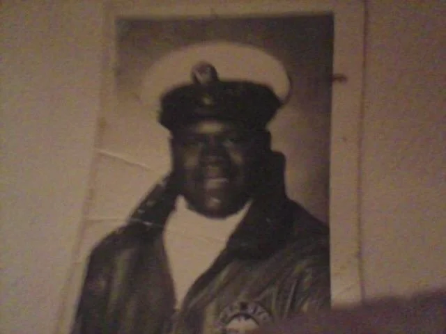 A black and white photo of a man in a military uniform and cap, smiling. Benny Mobley Public Speaker Emcee Podcast Coach Washington training on on one mentorship
