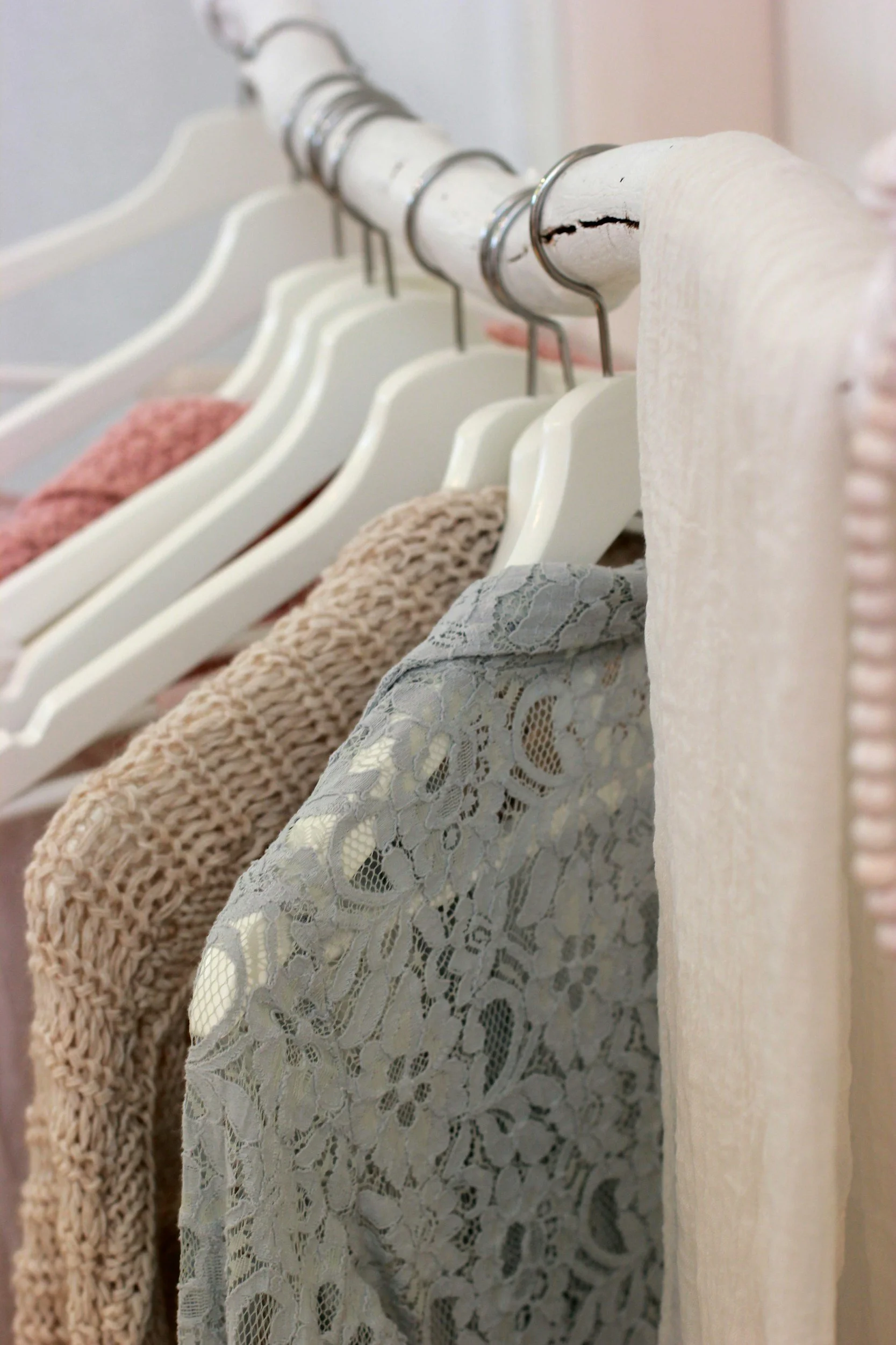 Close-up of a clothing rack with white hangers holding knitted and lace garments.