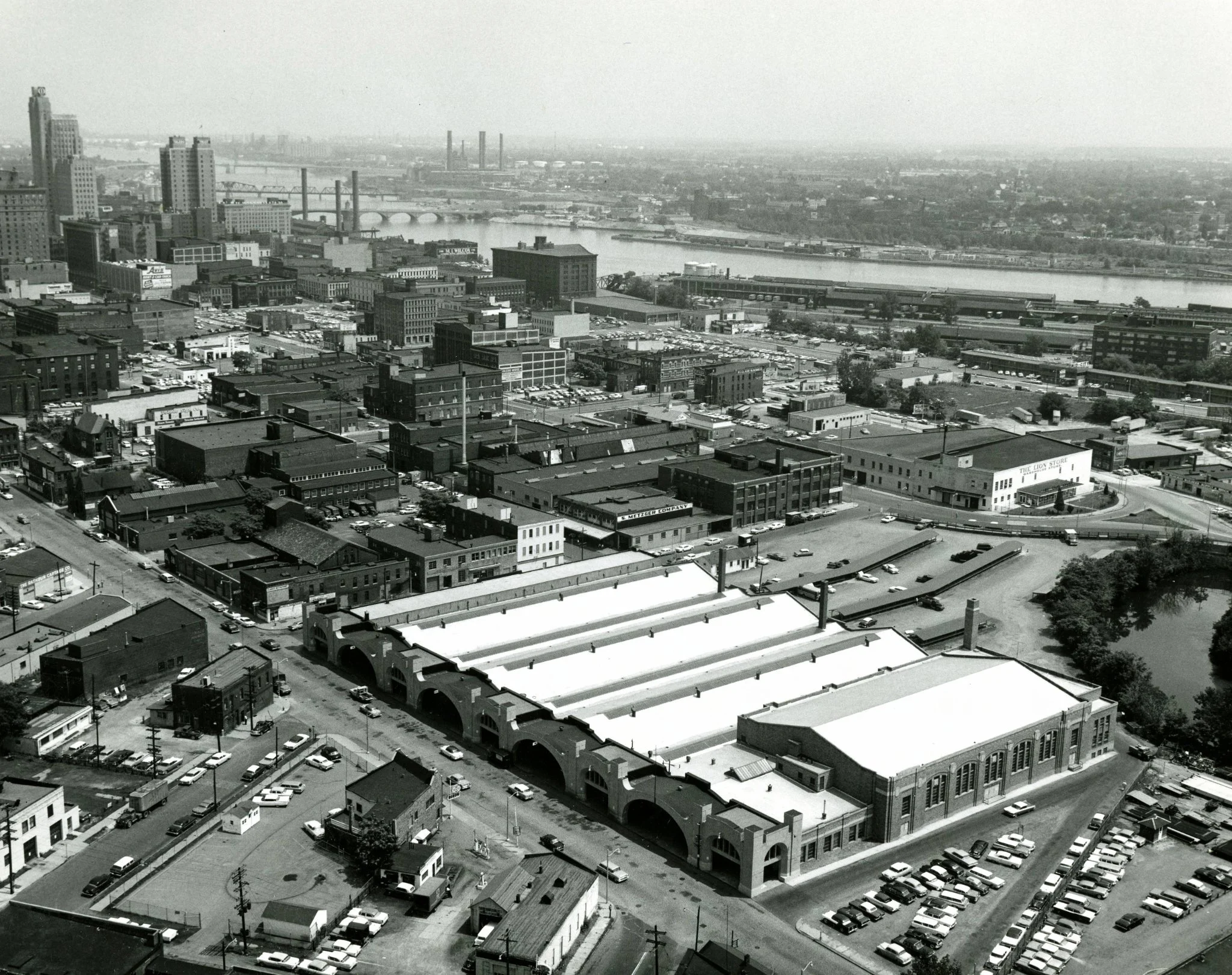 Black and white aerial view of a city with a mix of industrial and office buildings, a river, and bridges in the background.