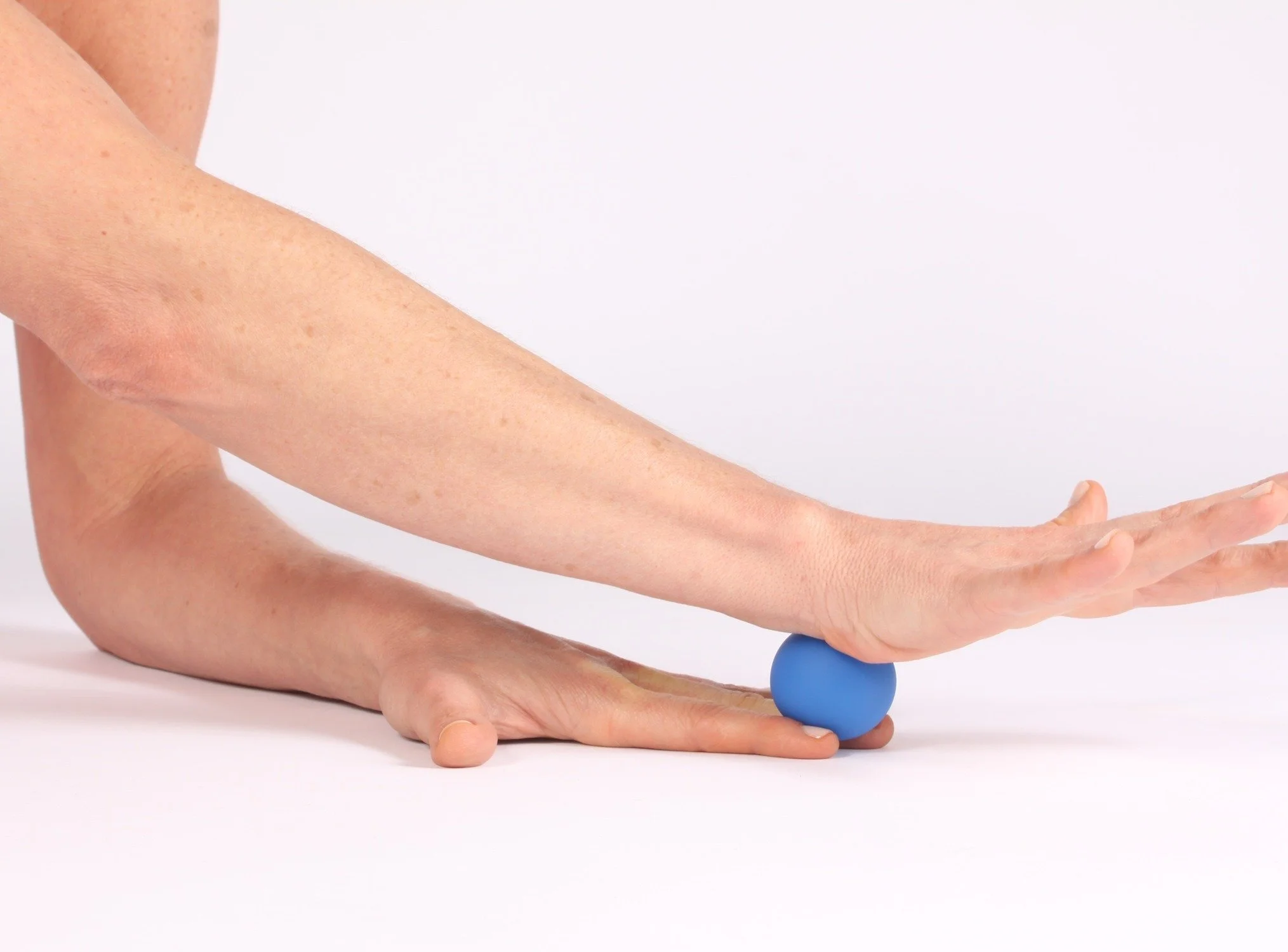 A person stretching with their right arm extended, palm down on a blue massage ball on the ground, against a plain white background.