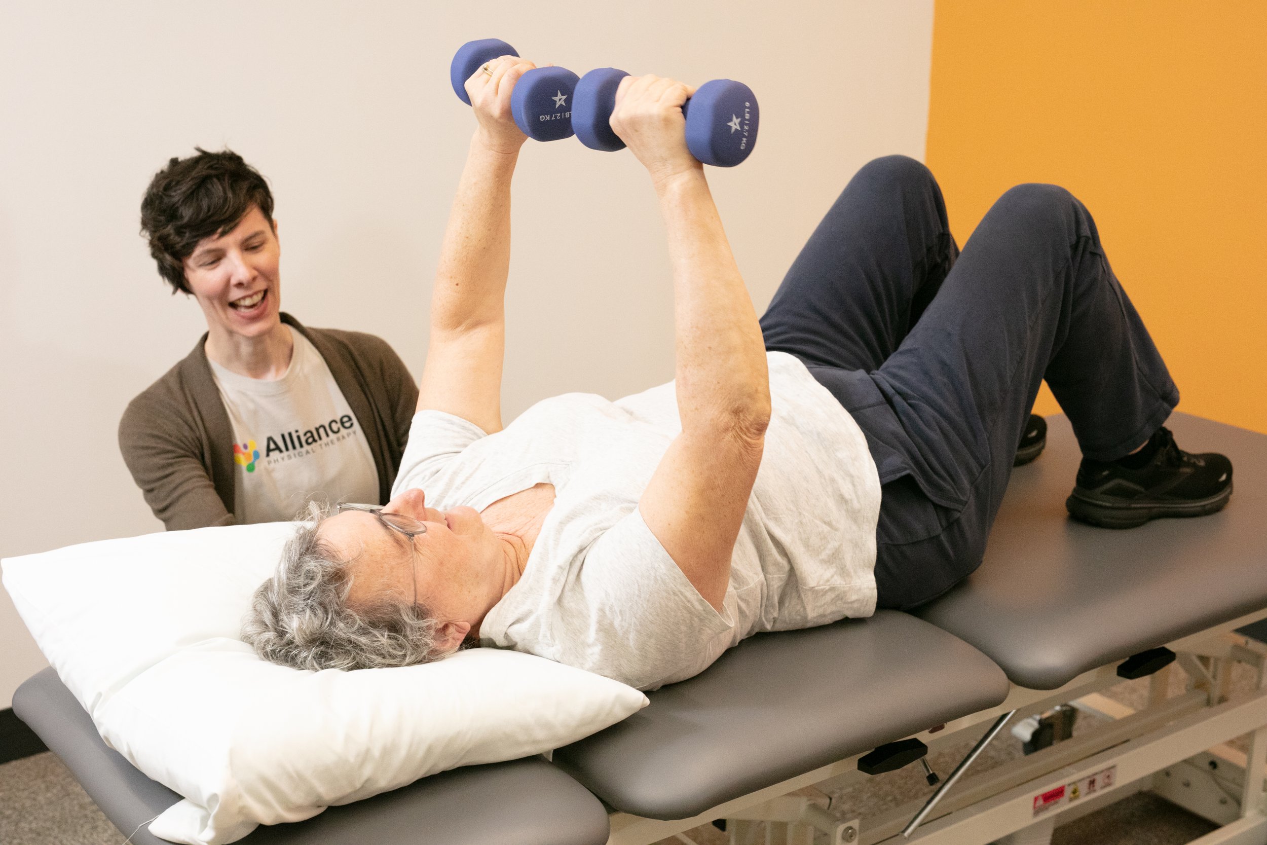 Trainer laughs with client lying down and lifting weights