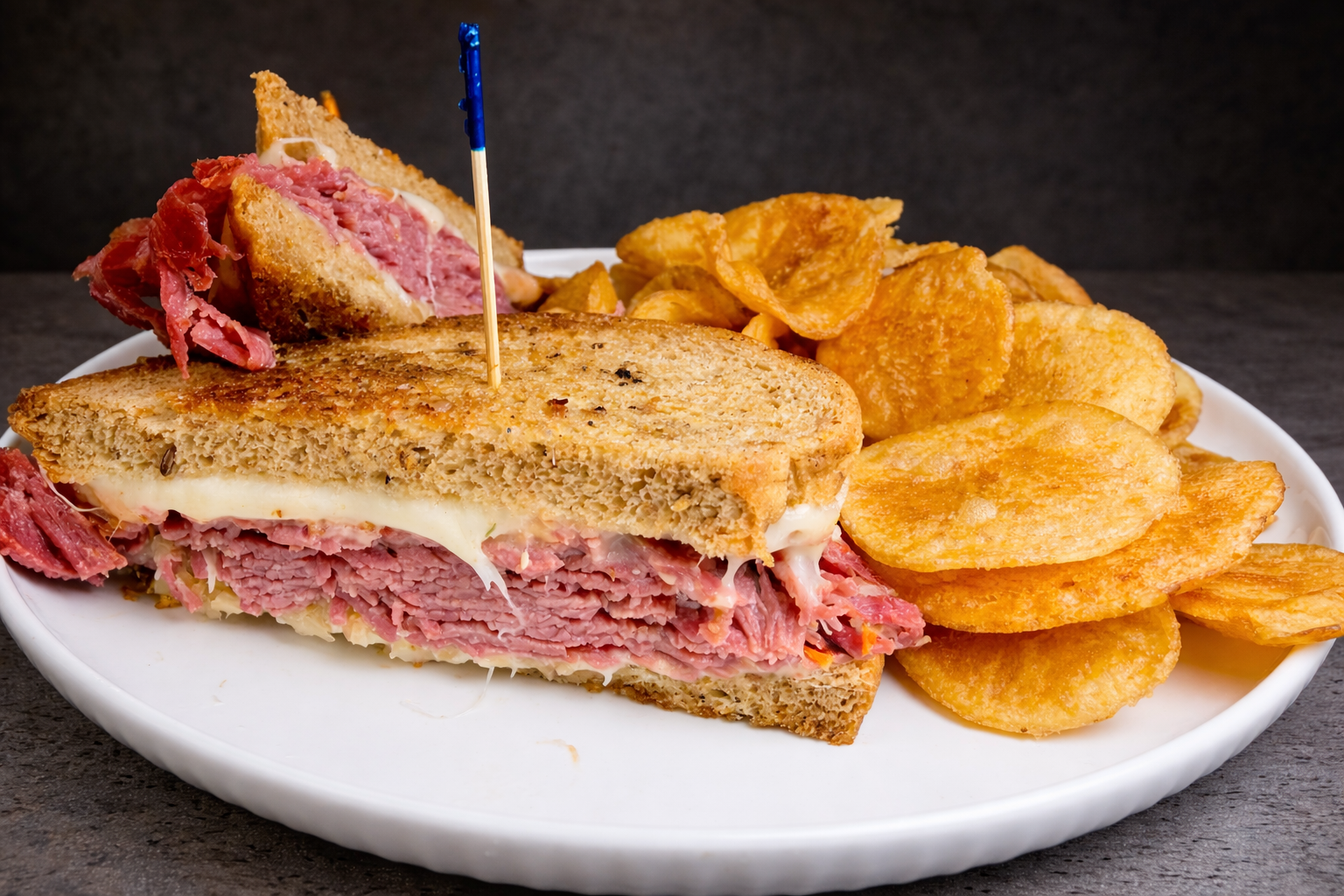 A plate of a triple-decker corned beef sandwich with melted cheese and a side of potato chips.