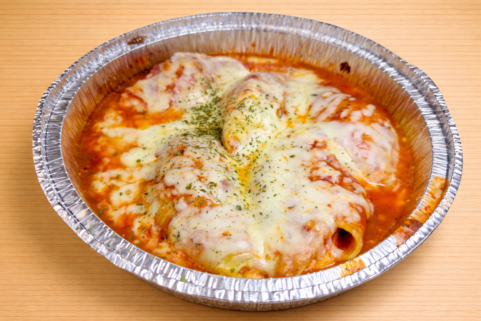 Baked manacotti pasta with tomato sauce and melted cheese in a disposable aluminum tray.