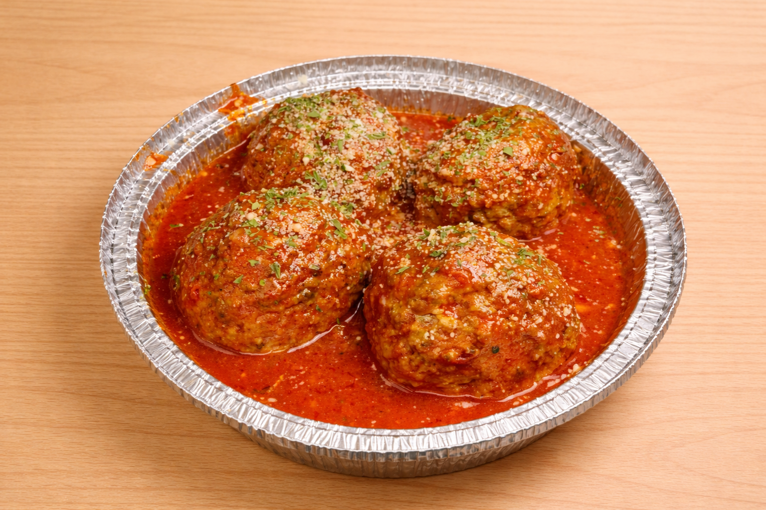Four meatballs in tomato sauce garnished with chopped herbs in a foil tray.