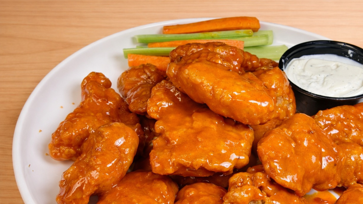 Plate of buffalo chicken wings with dipping sauce and vegetable sticks