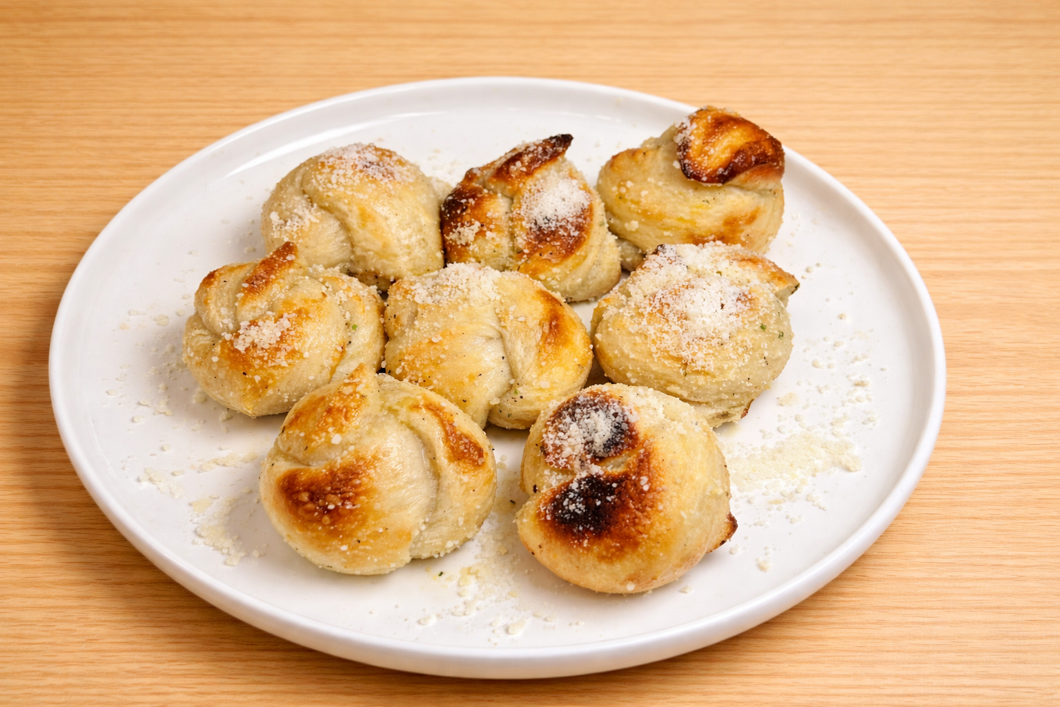 Plate of roasted dumplings sprinkled with grated cheese on a wooden surface.