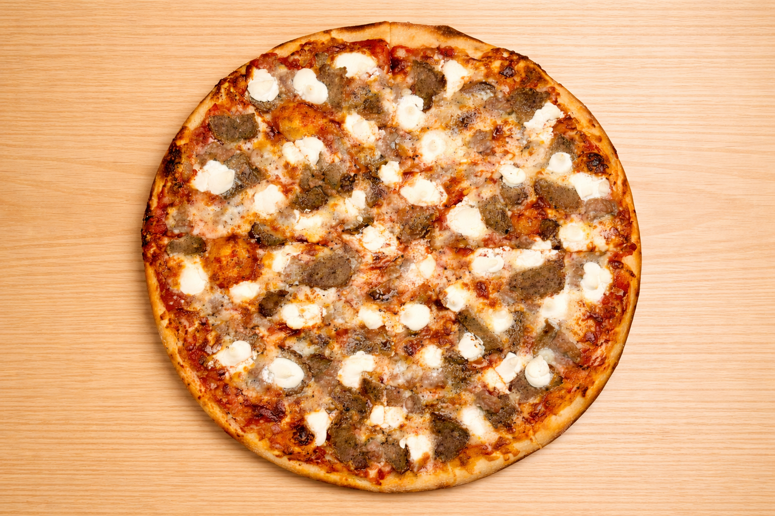 A whole pizza topped with cheese, sausage, and possibly other ingredients on a wooden surface.