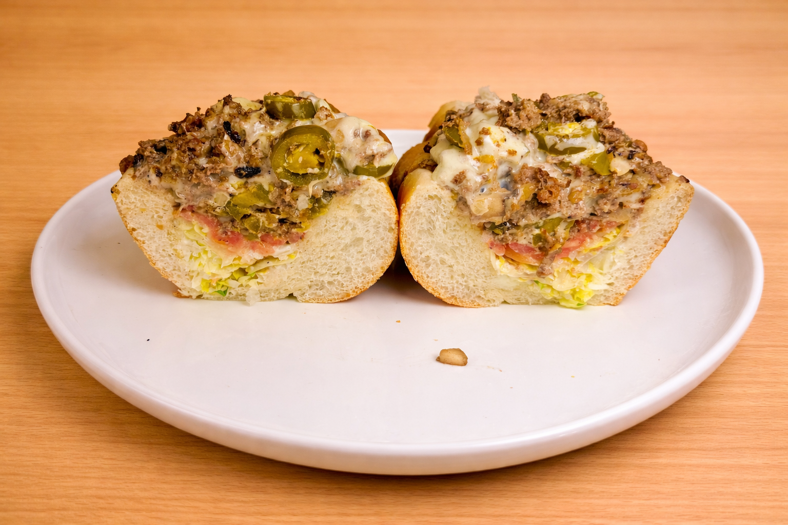 Half of a stuffed bread roll with layers of lettuce, tomato, ground meat, cheese, chopped green peppers, and mayonnaise on a white plate.