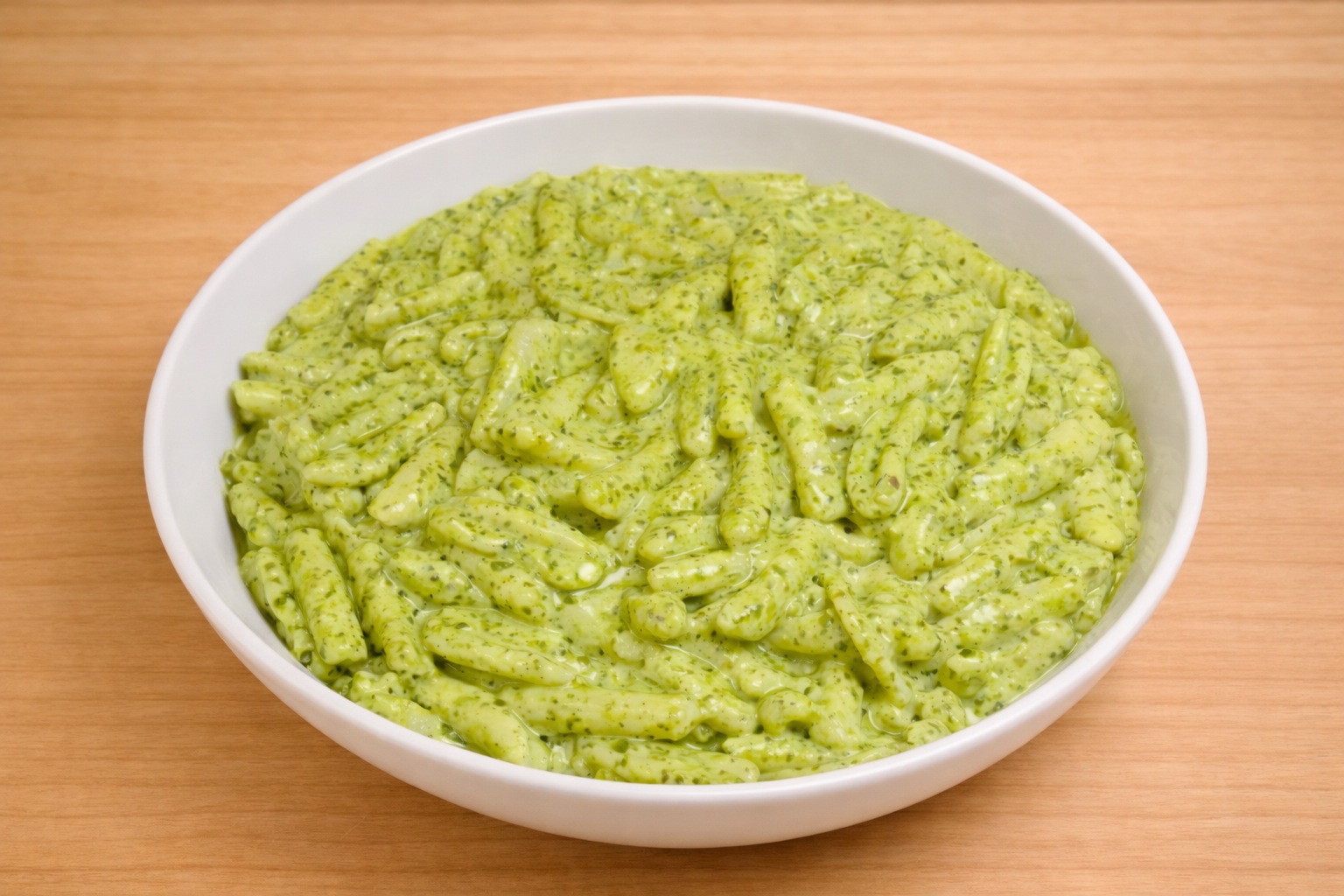 A white bowl filled with creamy, green pesto pasta on a wooden surface.