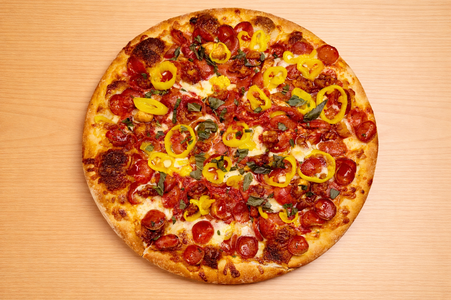 A pizza with pepperoni, sliced yellow bell peppers, chopped basil, and melted cheese on a light wooden surface.