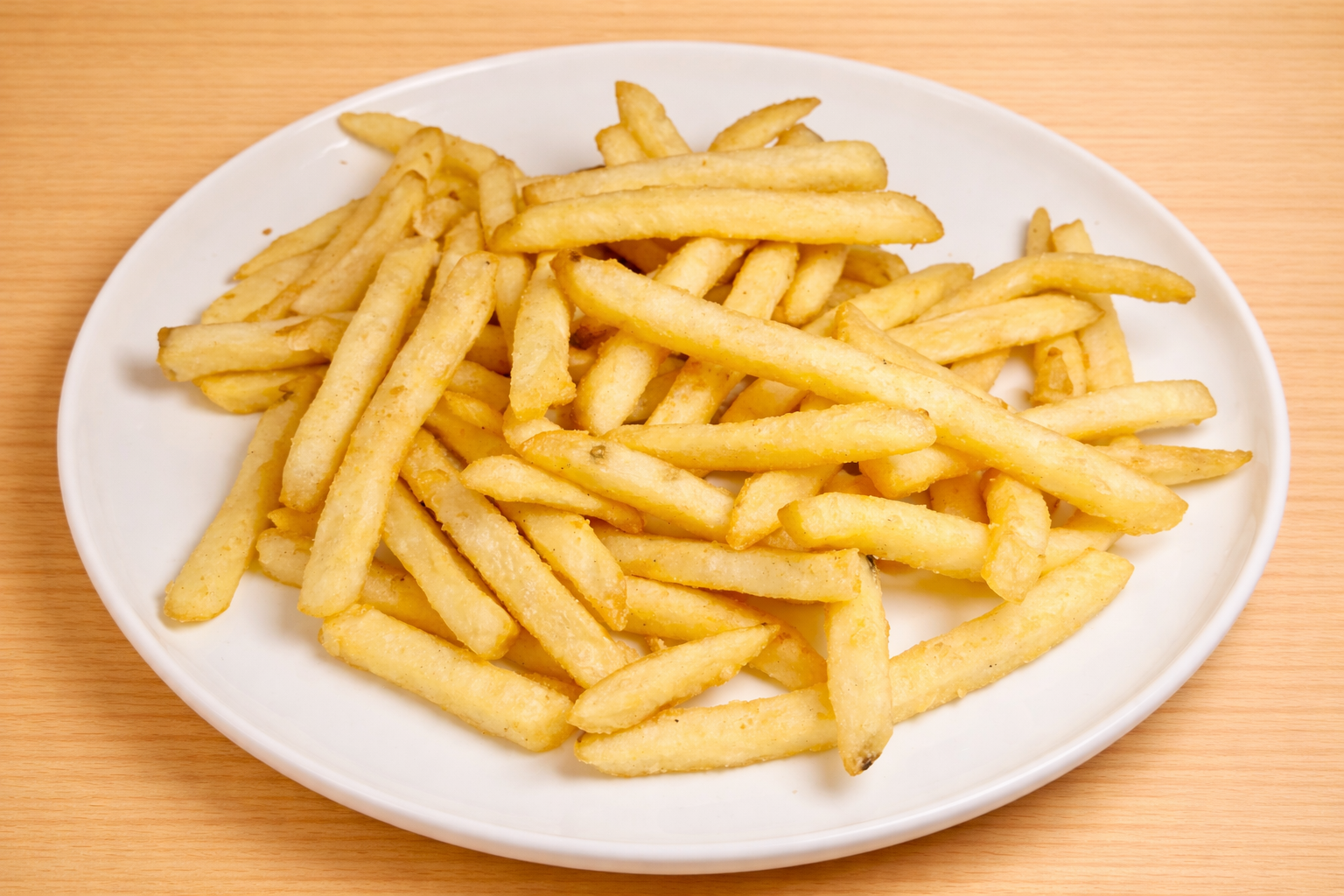 Pile of French fries on a white oval plate, resting on a wooden surface.