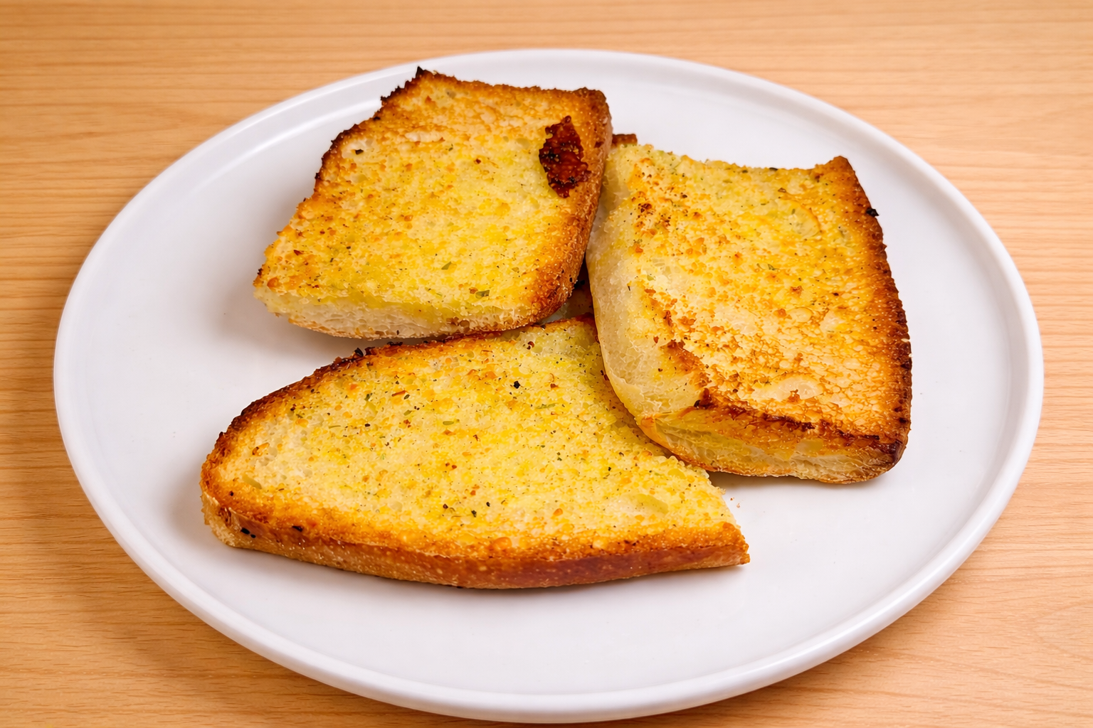Three slices of garlic bread on a white plate on a wooden surface.