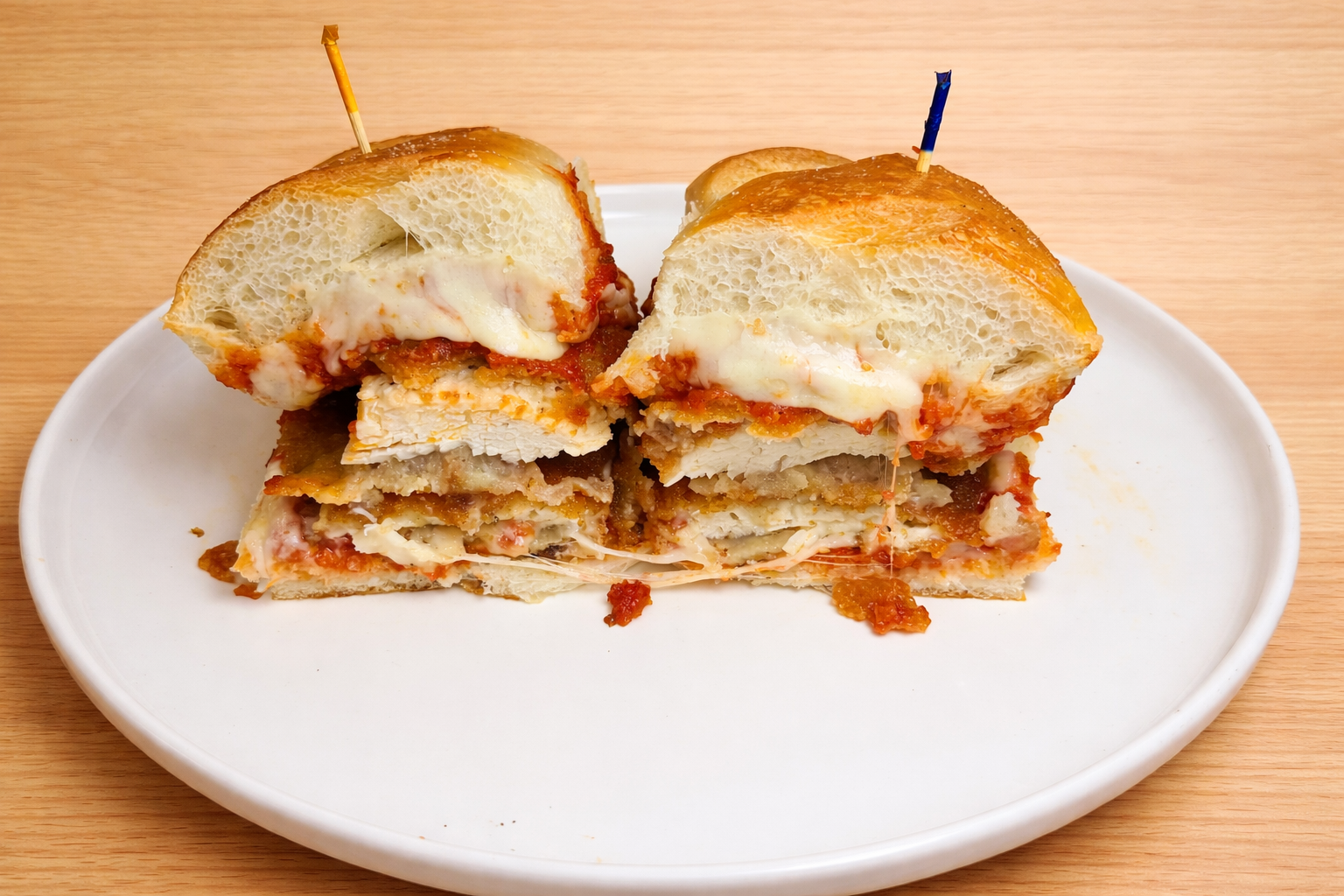 A white plate with slices of a stuffed bread, layered with cheese and tomato sauce, with toothpicks holding the slices together. The bread has a golden crust and is placed on a wooden surface.