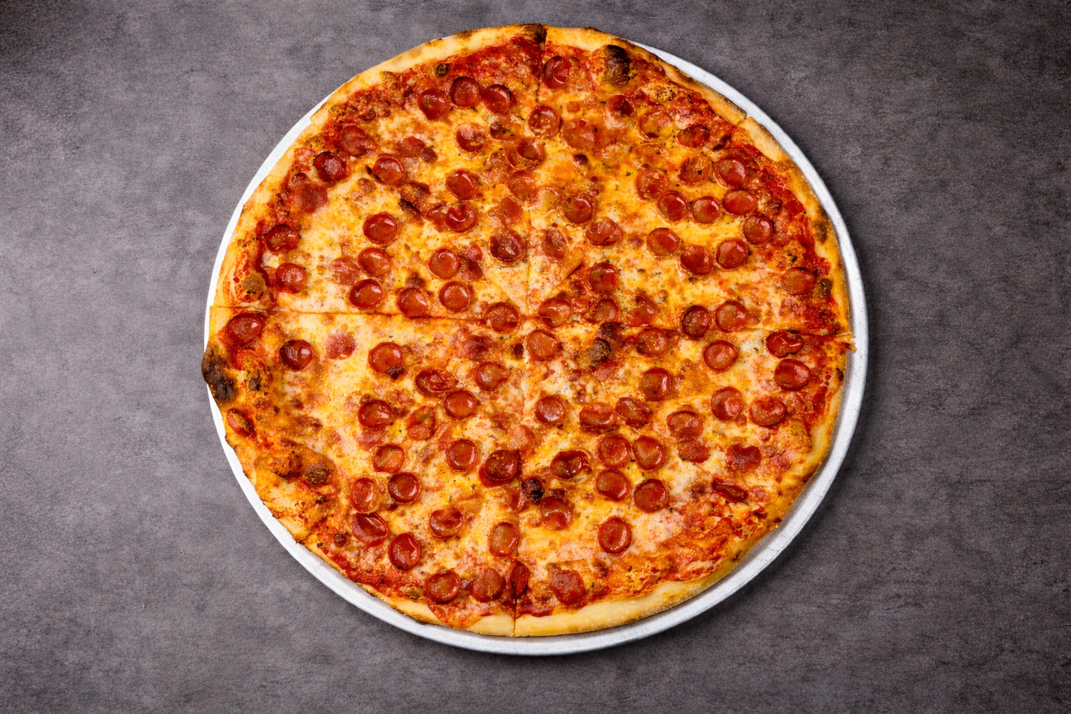 Round pepperoni pizza on a metal tray on gray surface, sliced, with cheese and tomato sauce.