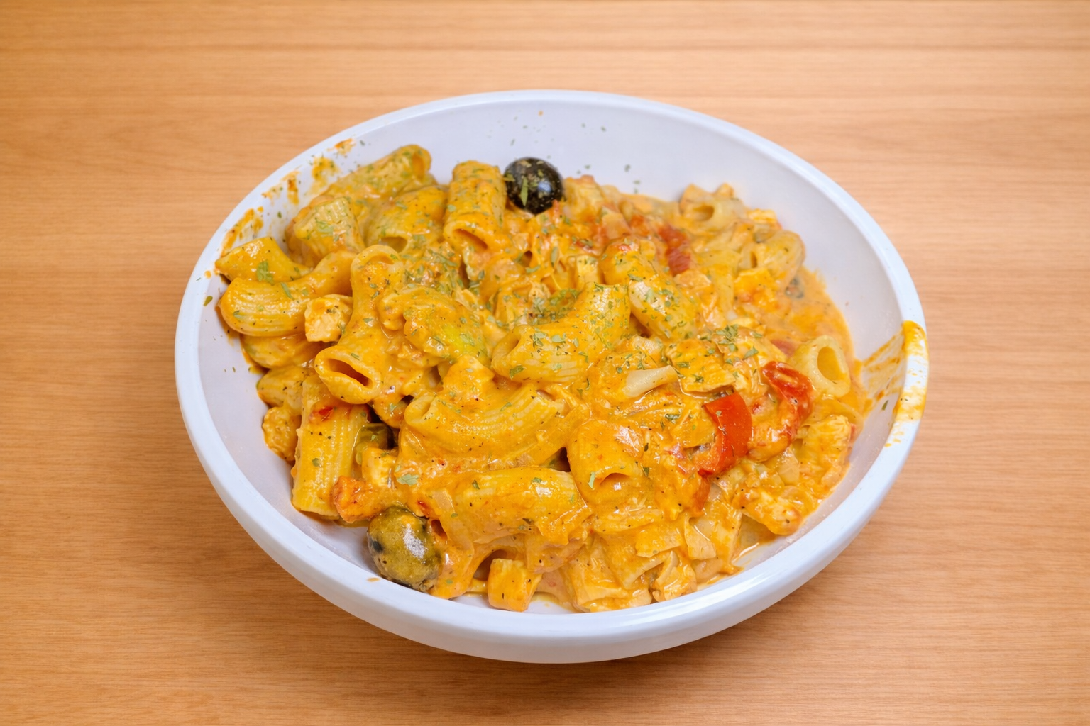 A white bowl of creamy pasta with vegetables on a wooden surface.