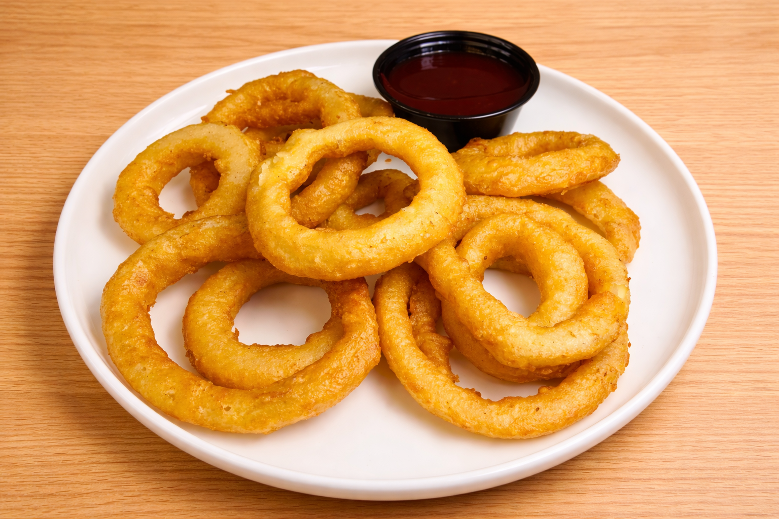 Fried onion rings with a small cup of dipping sauce on a white plate