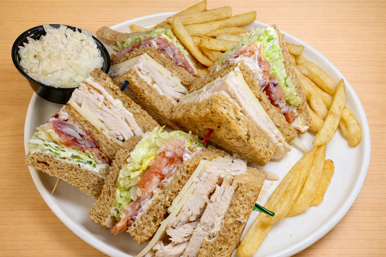 Club sandwich with turkey, lettuce, tomato, and cheese, served with French fries and coleslaw.