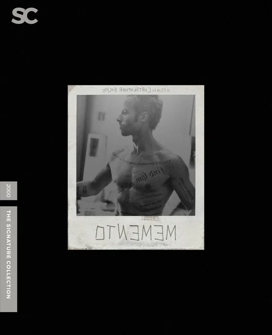 Black and white Polaroid photo of a shirtless man with tattoos on his chest and arm, looking to the side. The Polaroid has the text 'MEMENTO' written at the bottom. The photo is displayed against a black background.