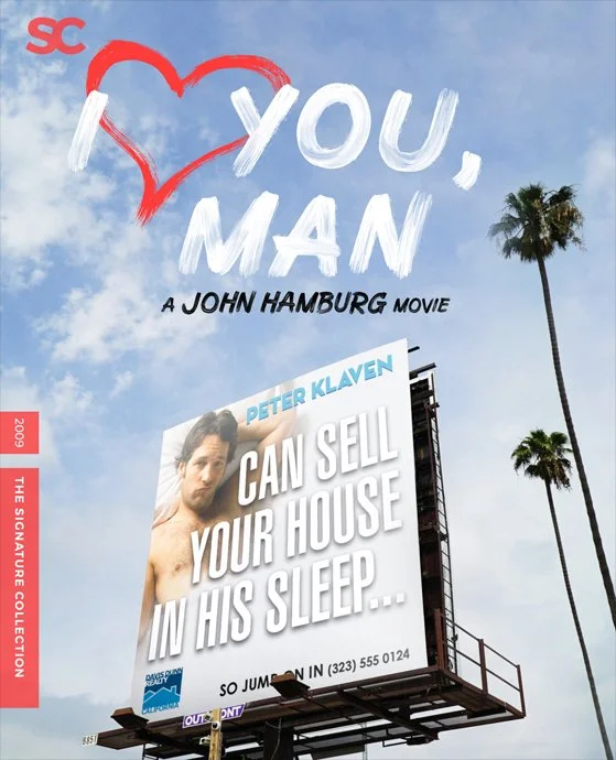 Billboard with a movie poster and sky background showing palm trees. The movie is titled "I Love You, Man" with the subtitle "A John Hamburg Movie." The billboard features a large image of a man, with text that says "Can Sell Your House In His Sleep.