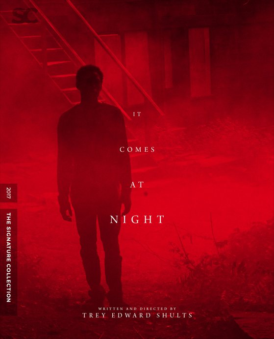 A person standing in a hazy setting witha red overlay, with the text "It Comes At Night" and "Written and Directed by Trey Edward Shults".