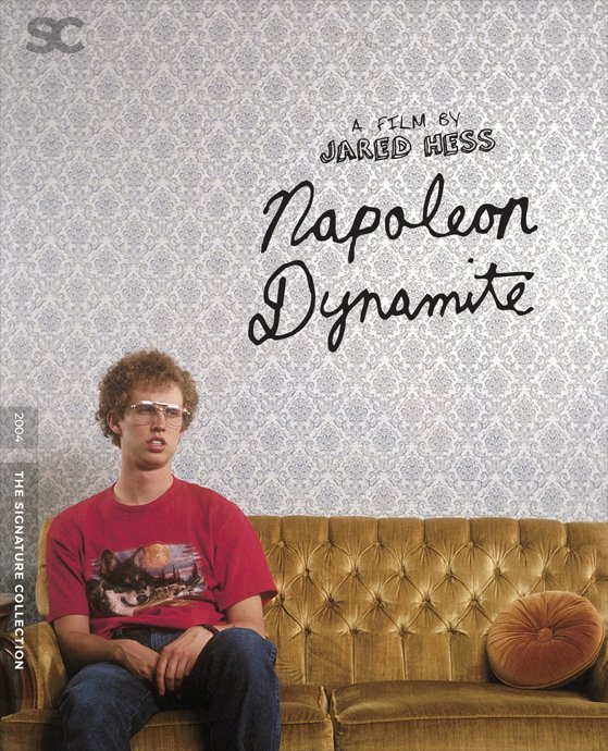 Promotional poster for the 2004 film "Napoleon Dynamite" featuring a young man with curly hair and glasses sitting on a yellow velvet couch with a round orange pillow, against a patterned wallpaper background.