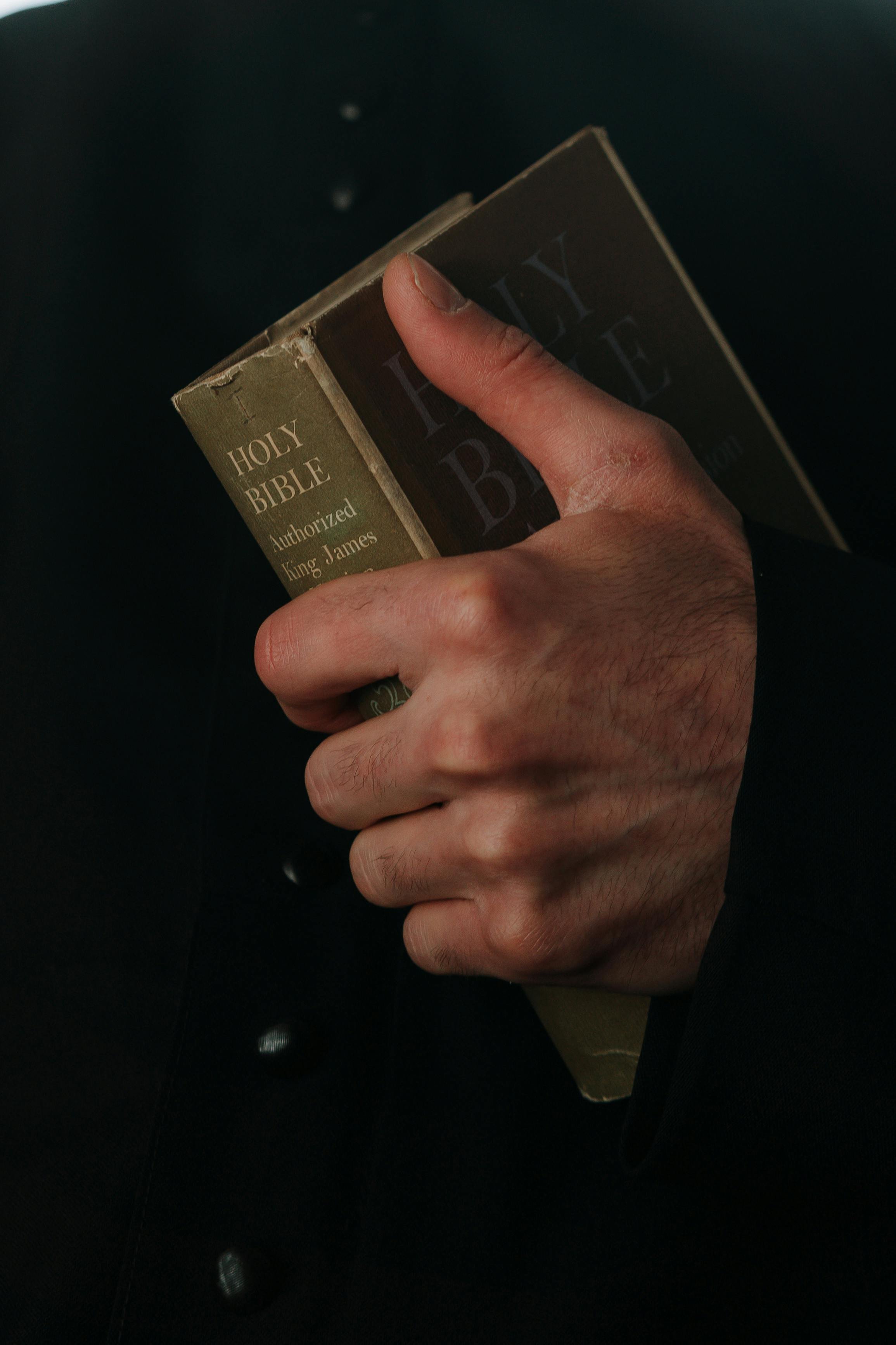 Close-up of a hand holding a Bible, with a dark background.