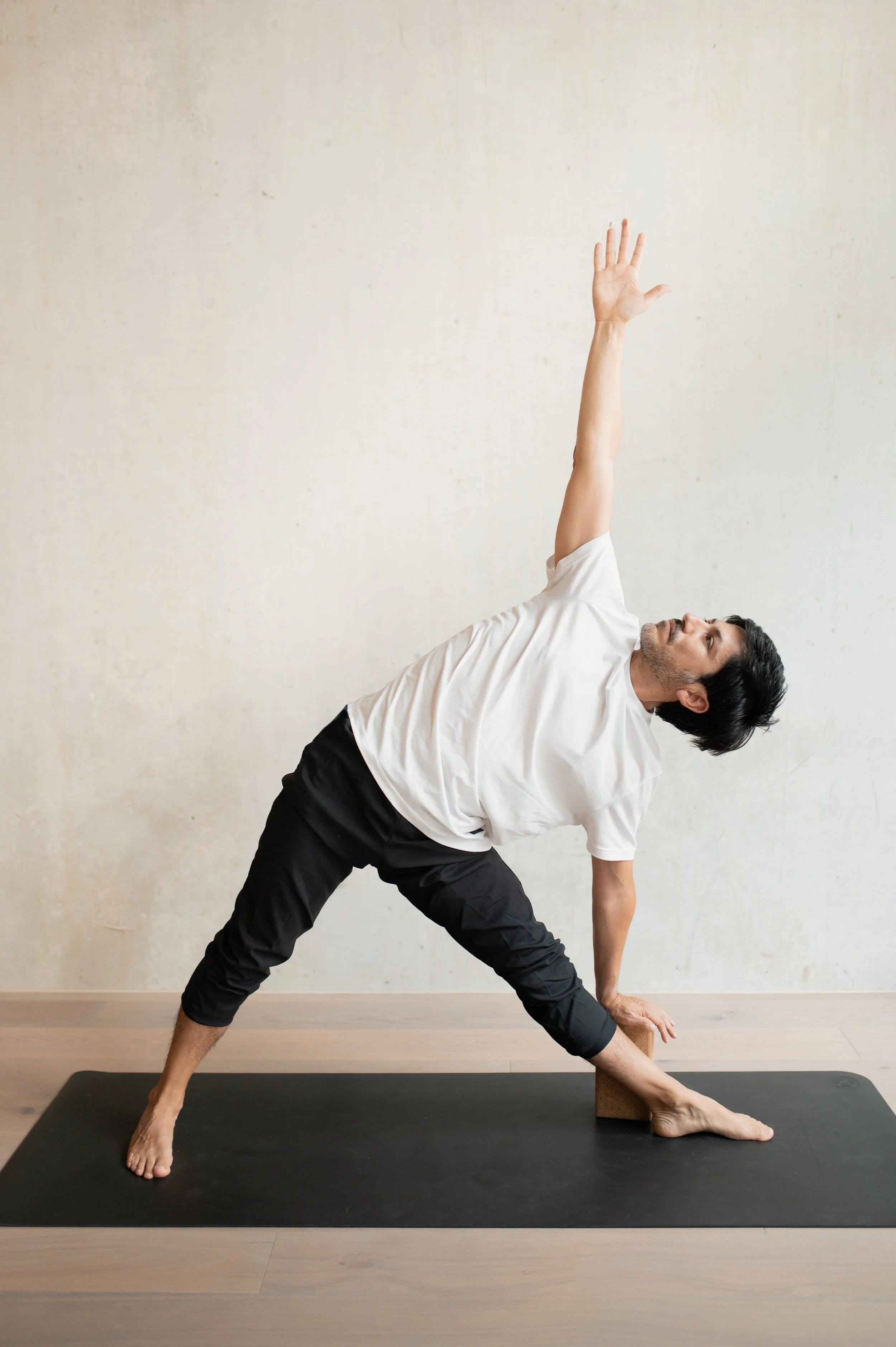 A man in a white t-shirt and black pants doing yoga in a triangle pose.