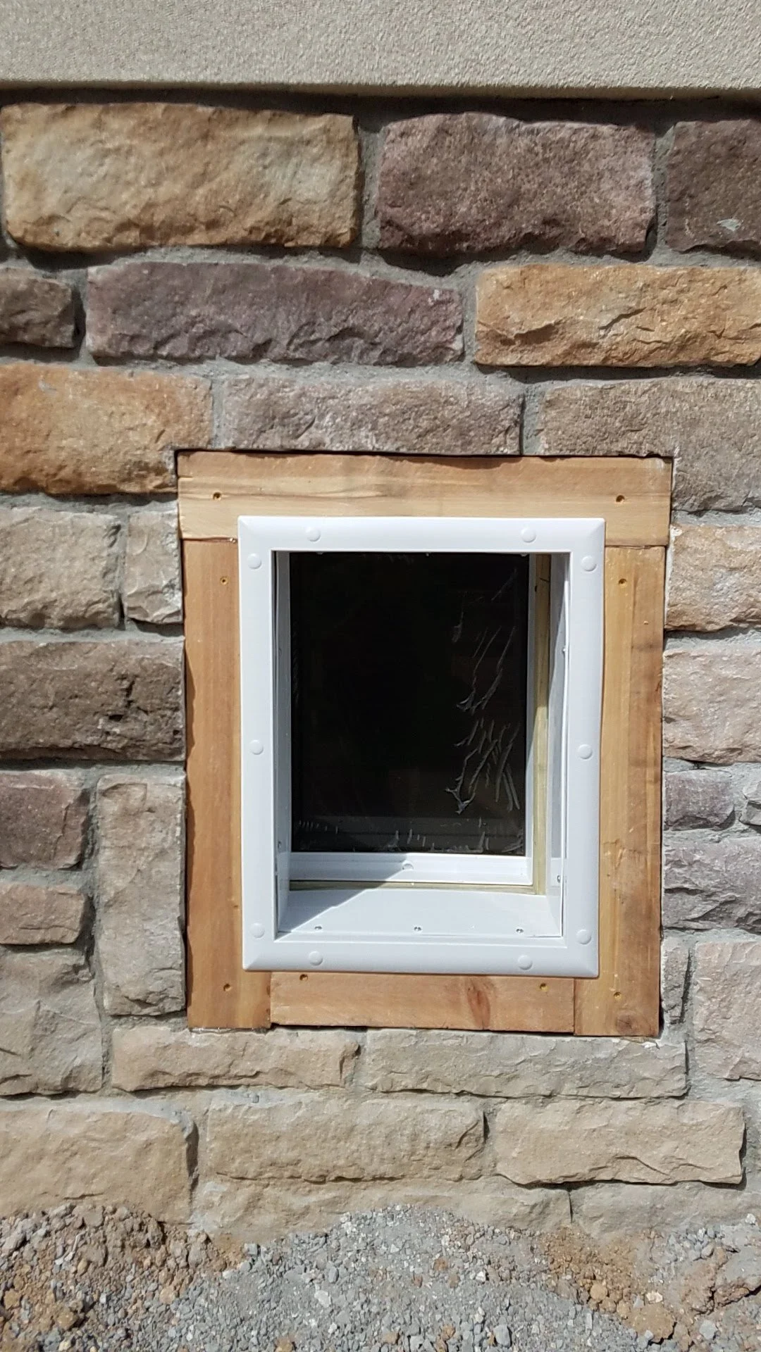 Close-up of a small pet door installed in a stone wall with a wooden frame around it.