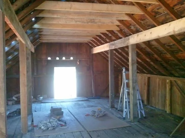 Interior of an 1800's barn with added purlins to repair sagging, overspanned rafters and beams, ladder, and construction tools.