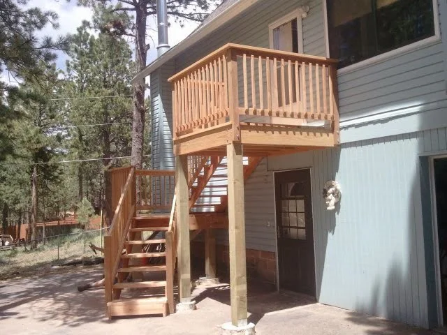 Wooden staircase leading to an elevated balcony attached to a house with white siding and a black door.